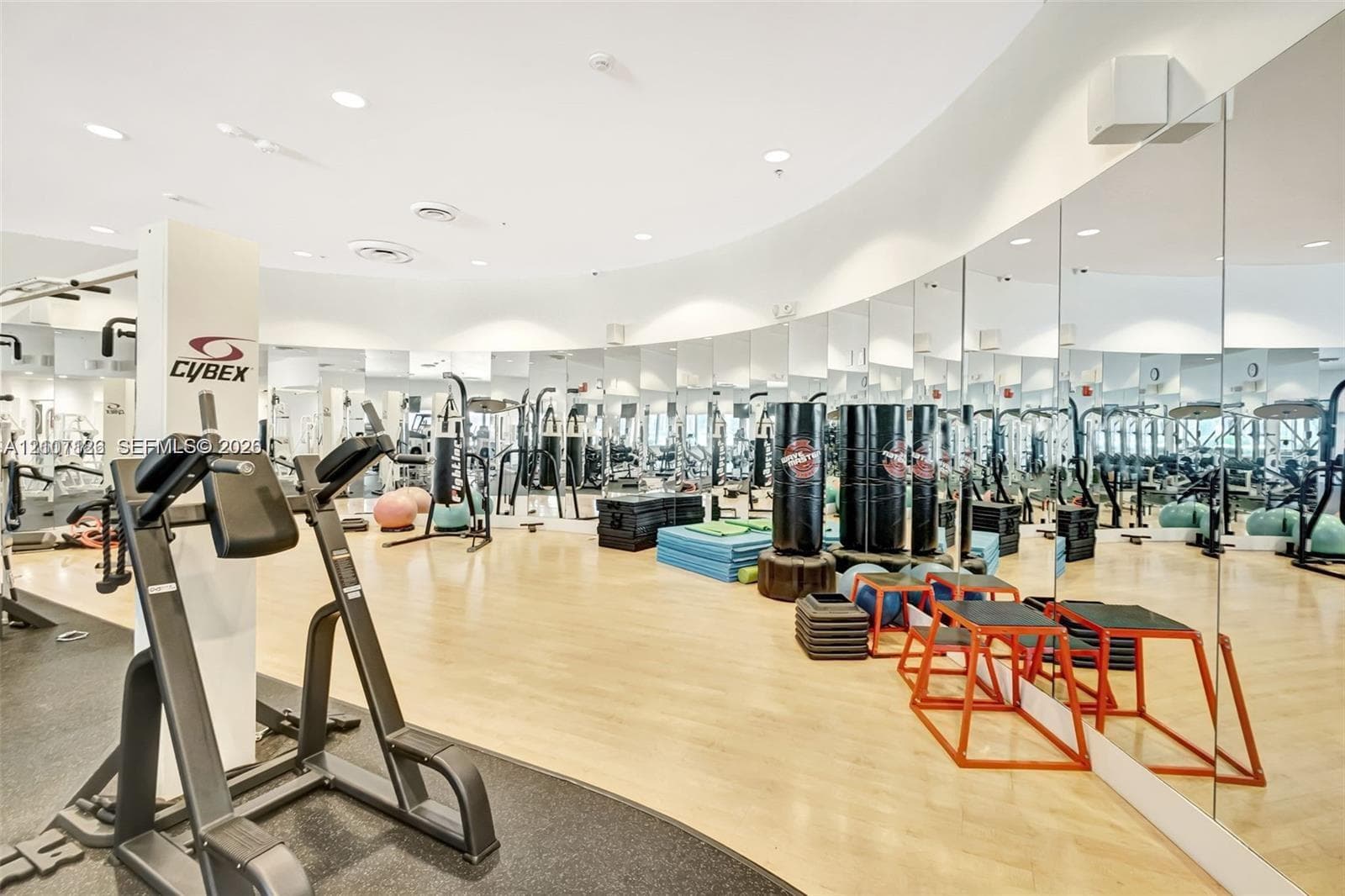 Fitness facility featuring floor-to-ceiling wall mirrors, wood-finish flooring, recessed lighting, and a curved architectural wall