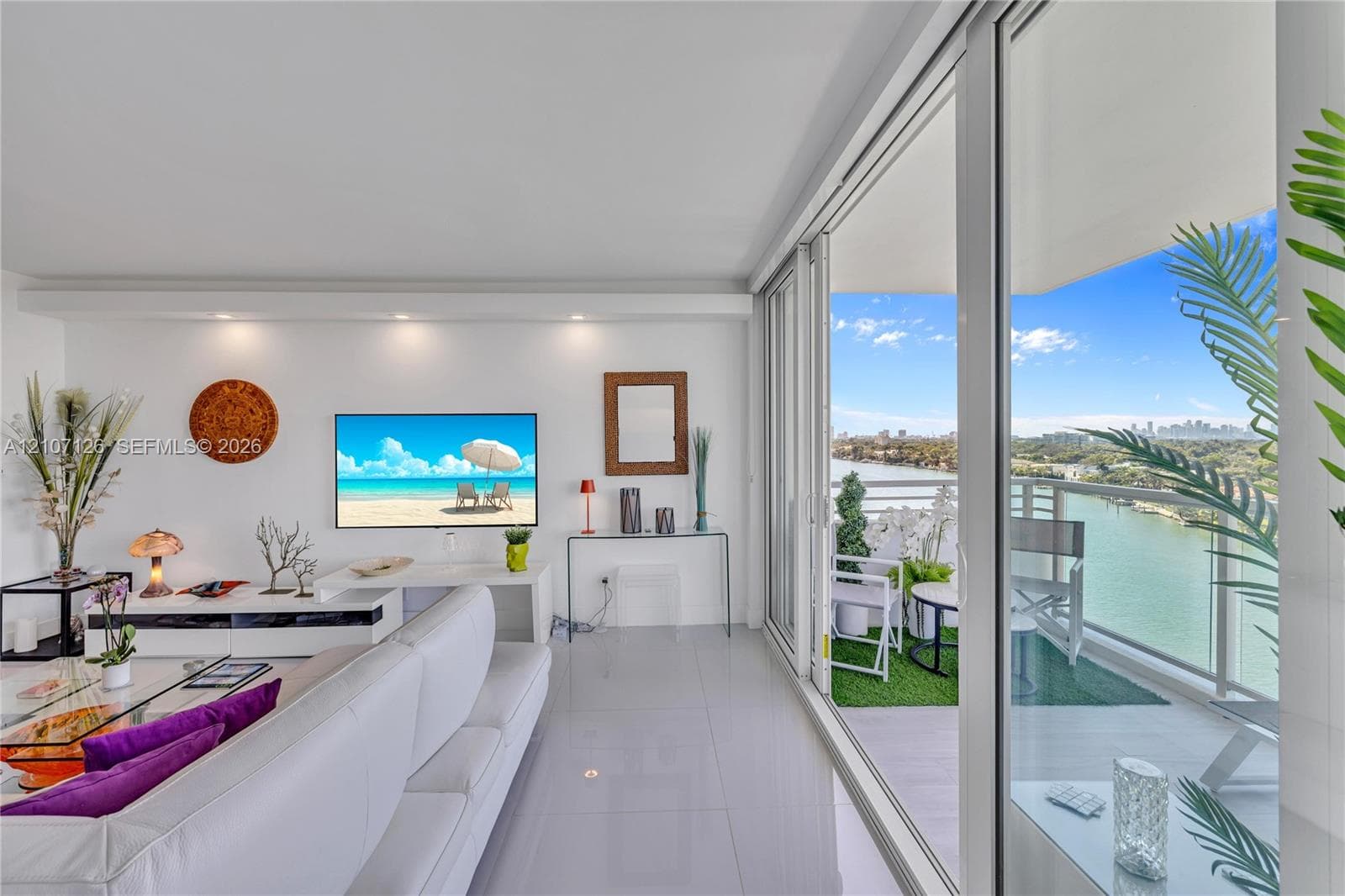 Open-concept living space featuring neutral large-format tile flooring, recessed ceiling lighting, and floor-to-ceiling sliding glass doors opening to a private balcony with metal railing
