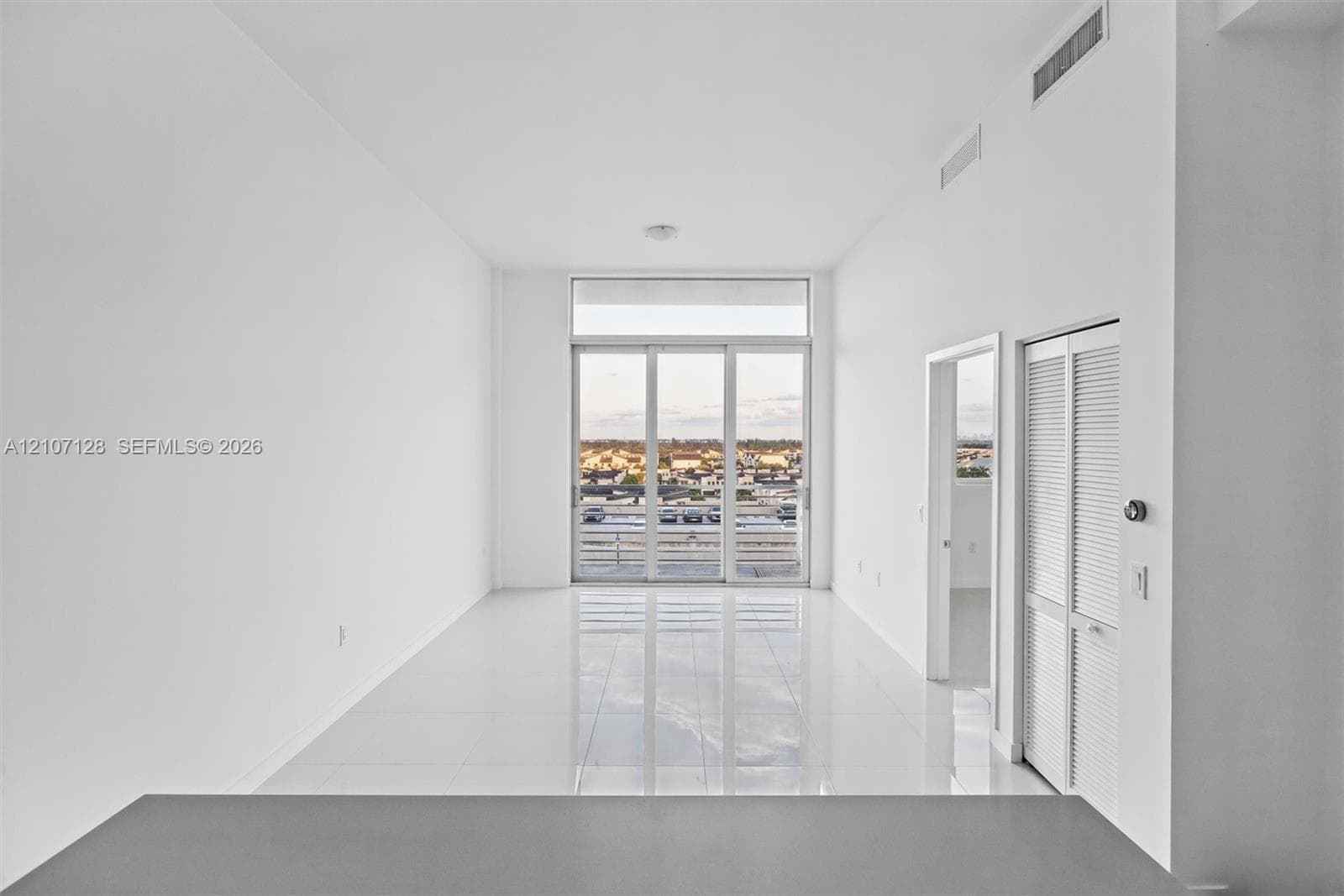Living area features high ceilings & full-height glass sliding doors, polished tile flooring, and louvered bifold closet doors
