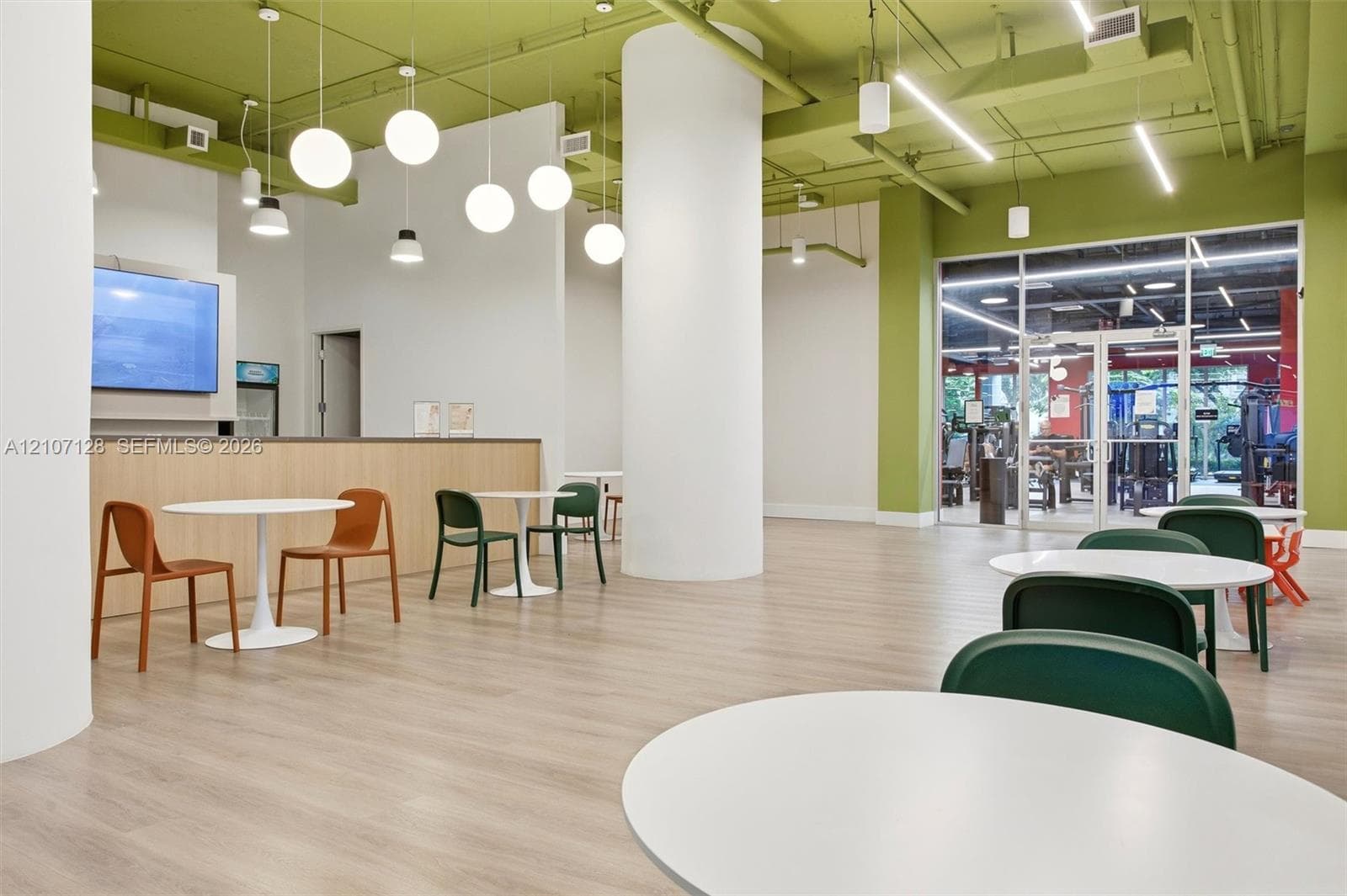 Open-concept space featuring wood-finish flooring, exposed industrial ceiling with pendant globe lighting, structural cylindrical columns, and full-height glass entry doors