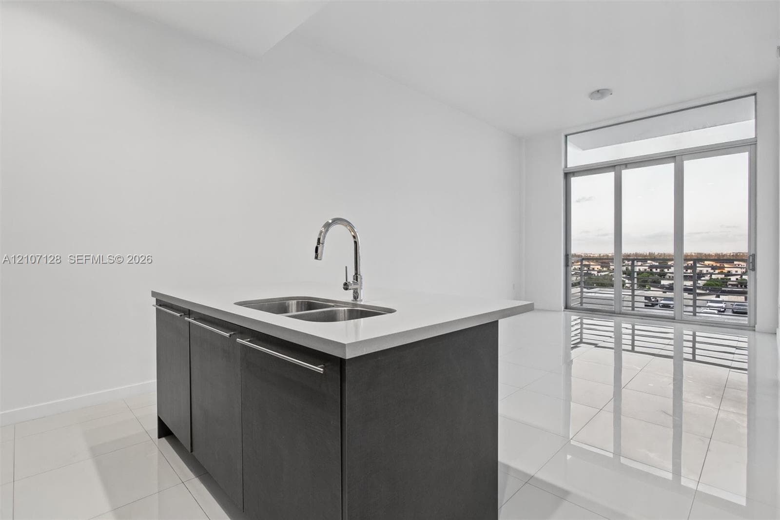 Center island featuring a stone countertop, dual-basin stainless steel sink, and high-arc chrome faucet, paired with dark cabinetry and polished tile flooring, highlighted by floor-to-ceiling glass sliding doors