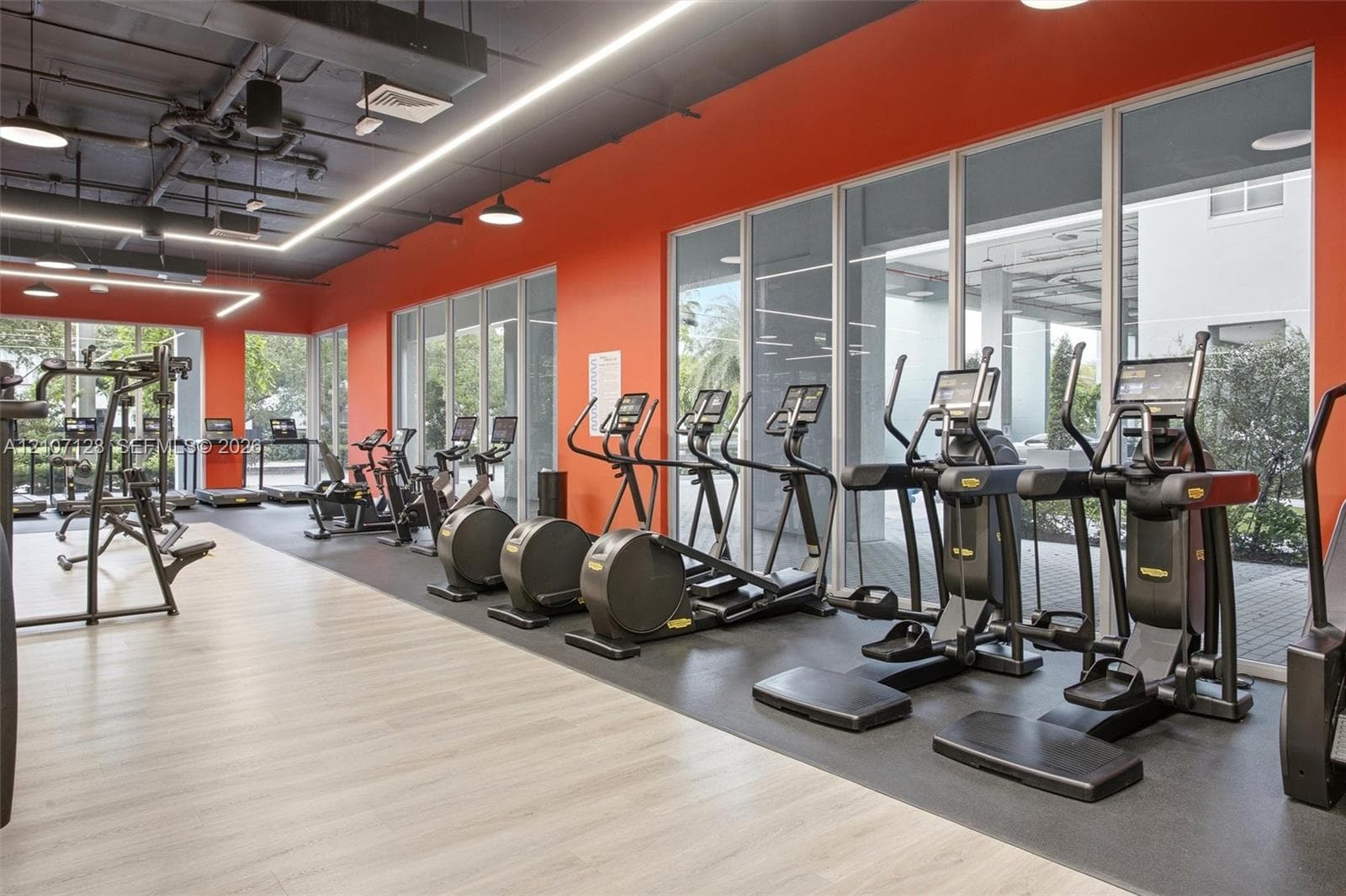 Fitness facility with modern exercise equipment, rubberized exercise surfacing, and an exposed industrial-style ceiling with recessed lighting