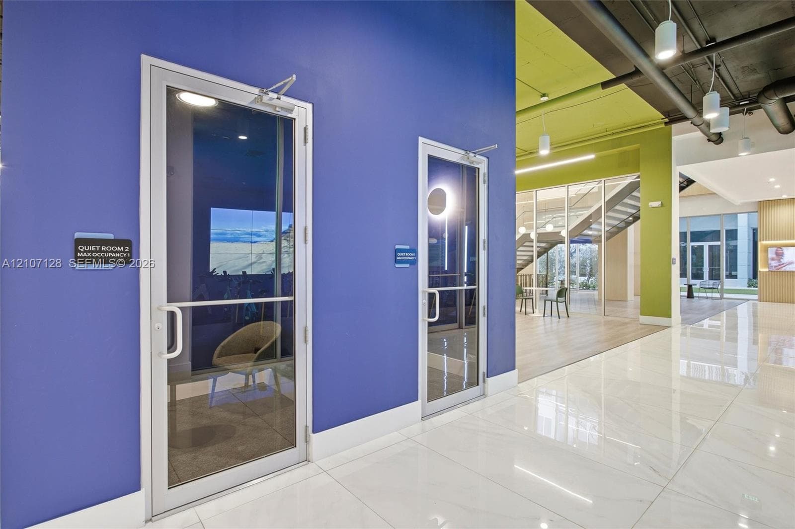 Enclosed glass-front rooms with polished tile flooring, contemporary color-blocked walls, exposed industrial-style ceilings, and pendant lighting