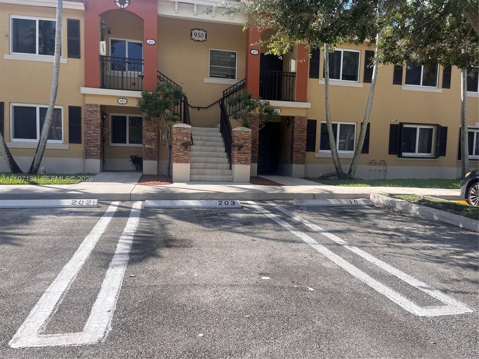 Two-story stucco exterior featuring stone veneer accents, decorative black shutters, metal railings, and reserved parking spaces