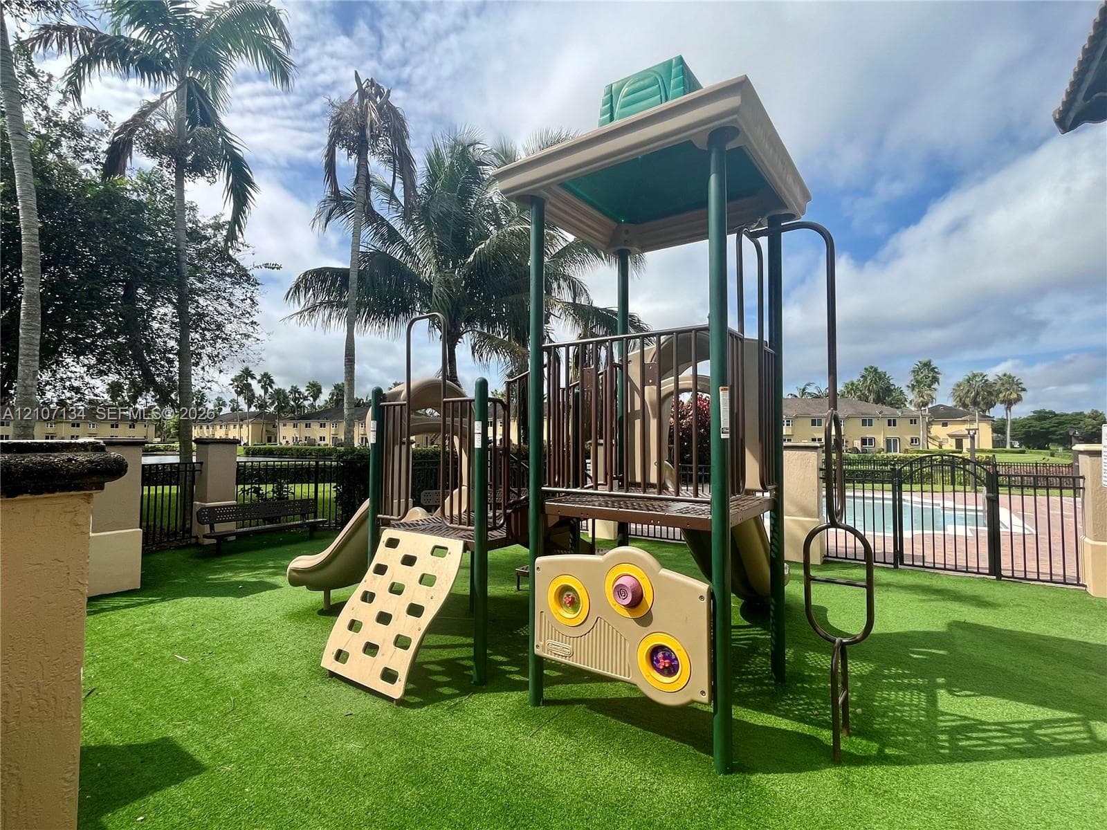 Playground structure featuring a climbing wall, slides, and activity panels situated on synthetic turf flooring