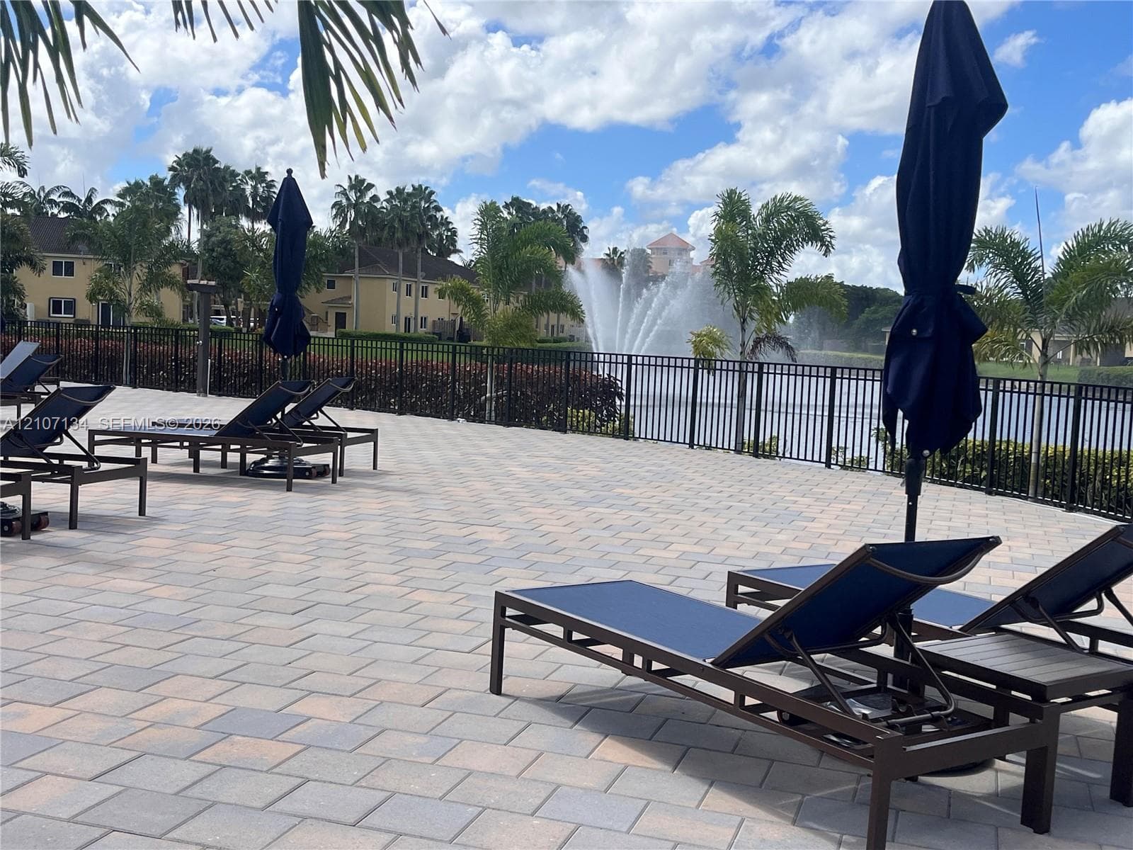 Paver-surfaced patio area featuring a metal perimeter fence and a water feature with a fountain