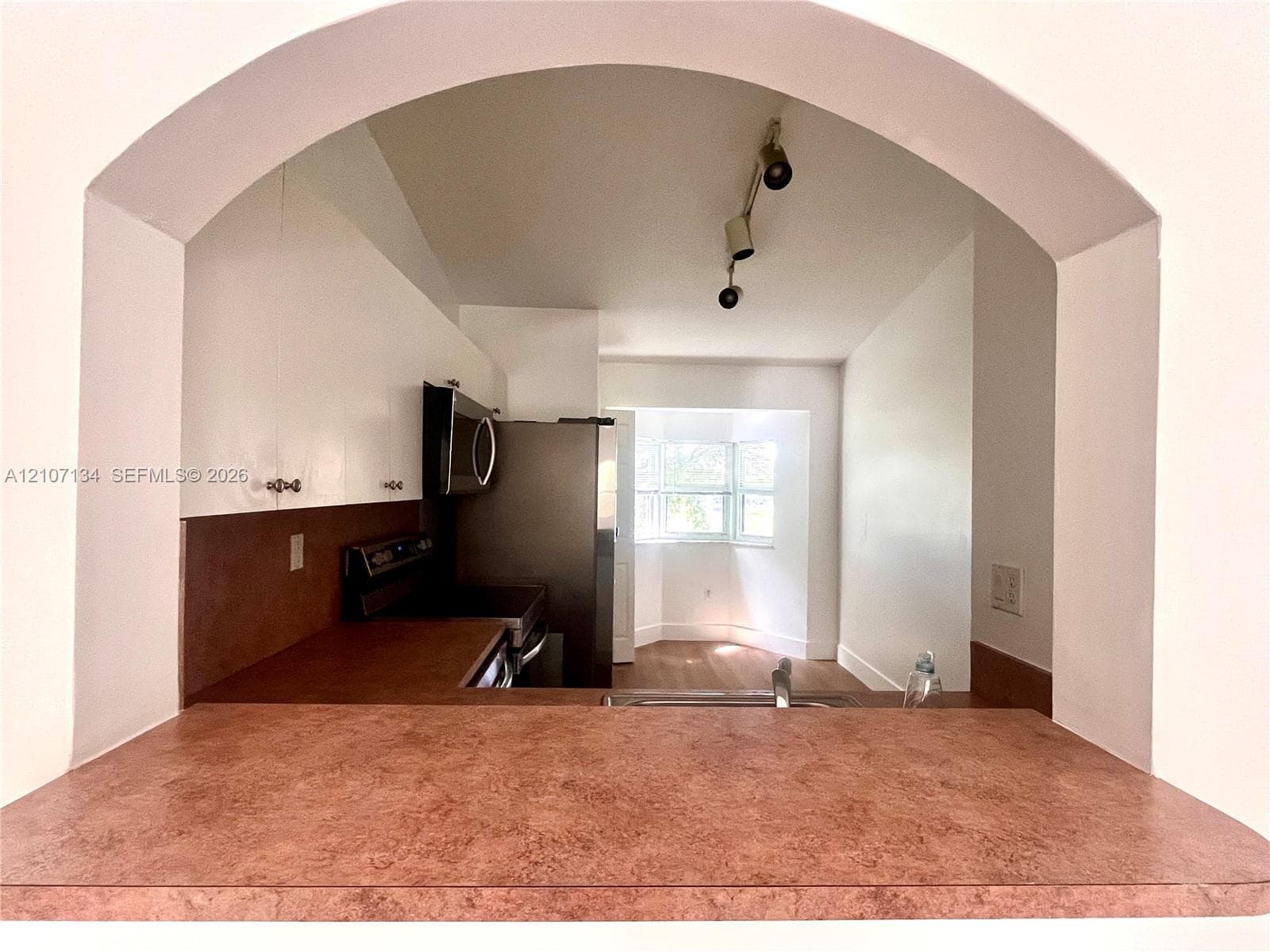 Arched pass-through featuring a textured countertop, white cabinetry, stainless steel appliances, track lighting, and wood-finish flooring
