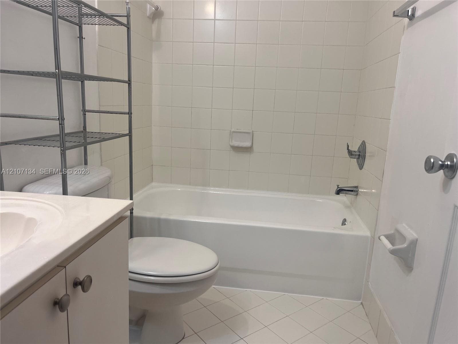 Bathroom featuring a white vanity with a composite countertop, an integrated sink, a porcelain soaking tub with tile surround, and diamond-pattern floor tiling