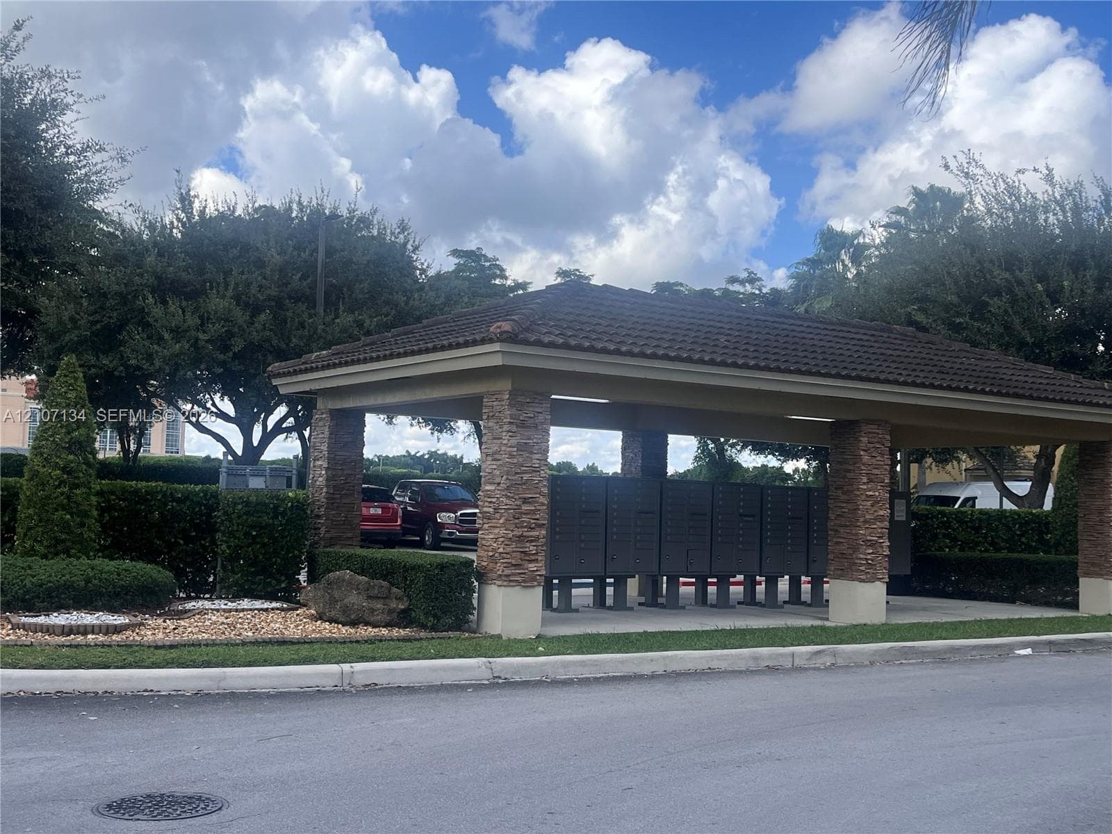 Covered mailbox station featuring a hipped tile roof, masonry stone pillars, and concrete pad