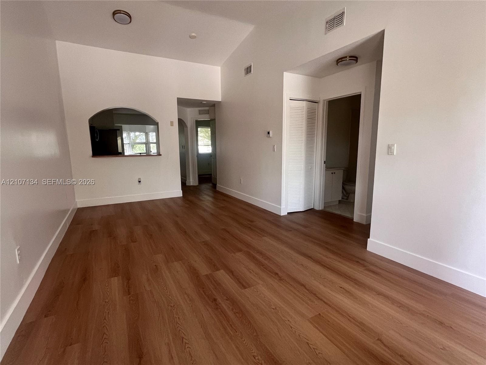 Vaulted ceilings, wood-finish flooring, and an arched pass-through window featuring a ledge