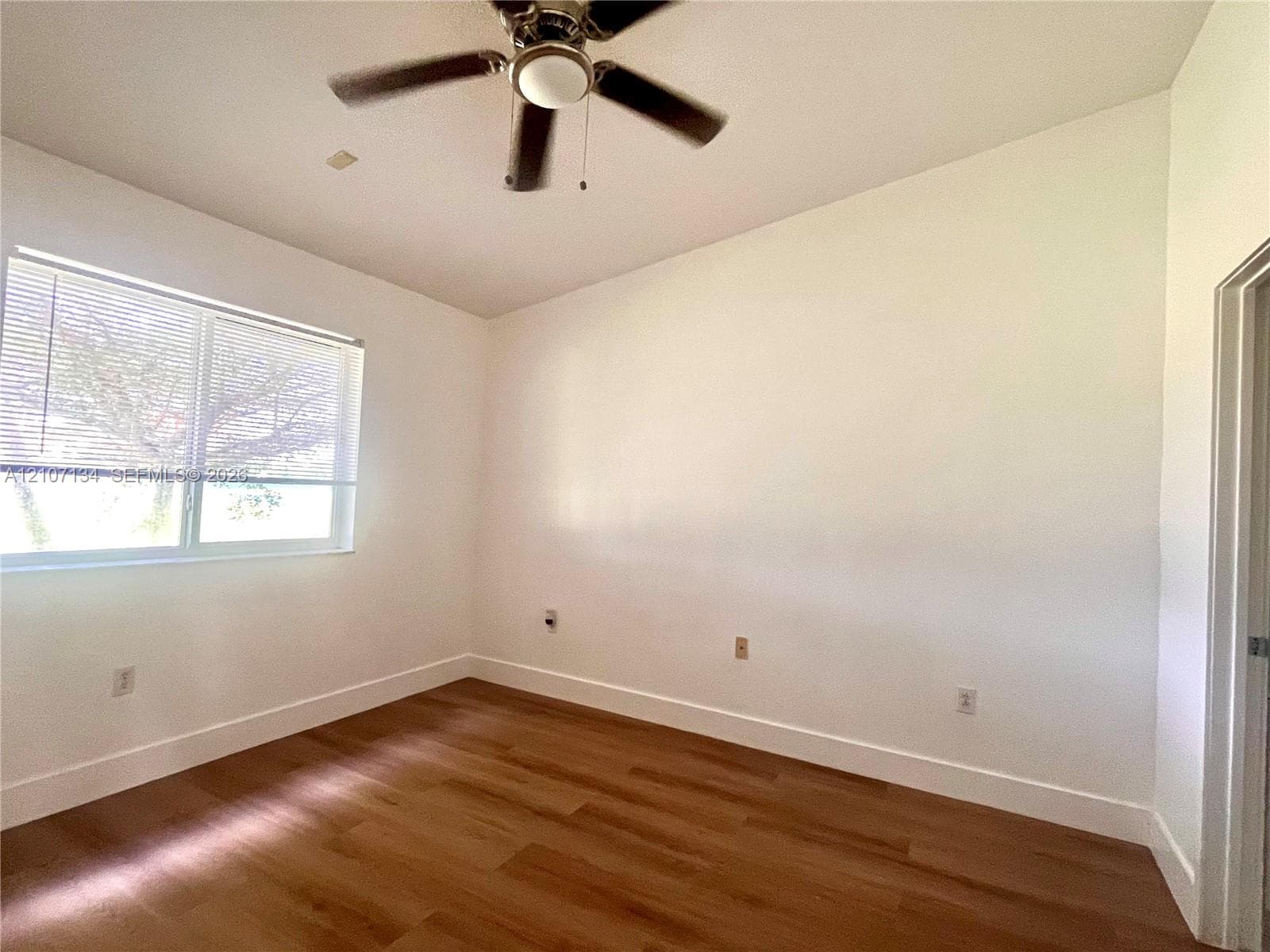 Neutral-toned room featuring wood-finish flooring, a ceiling fan with integrated lighting, and a large horizontal window