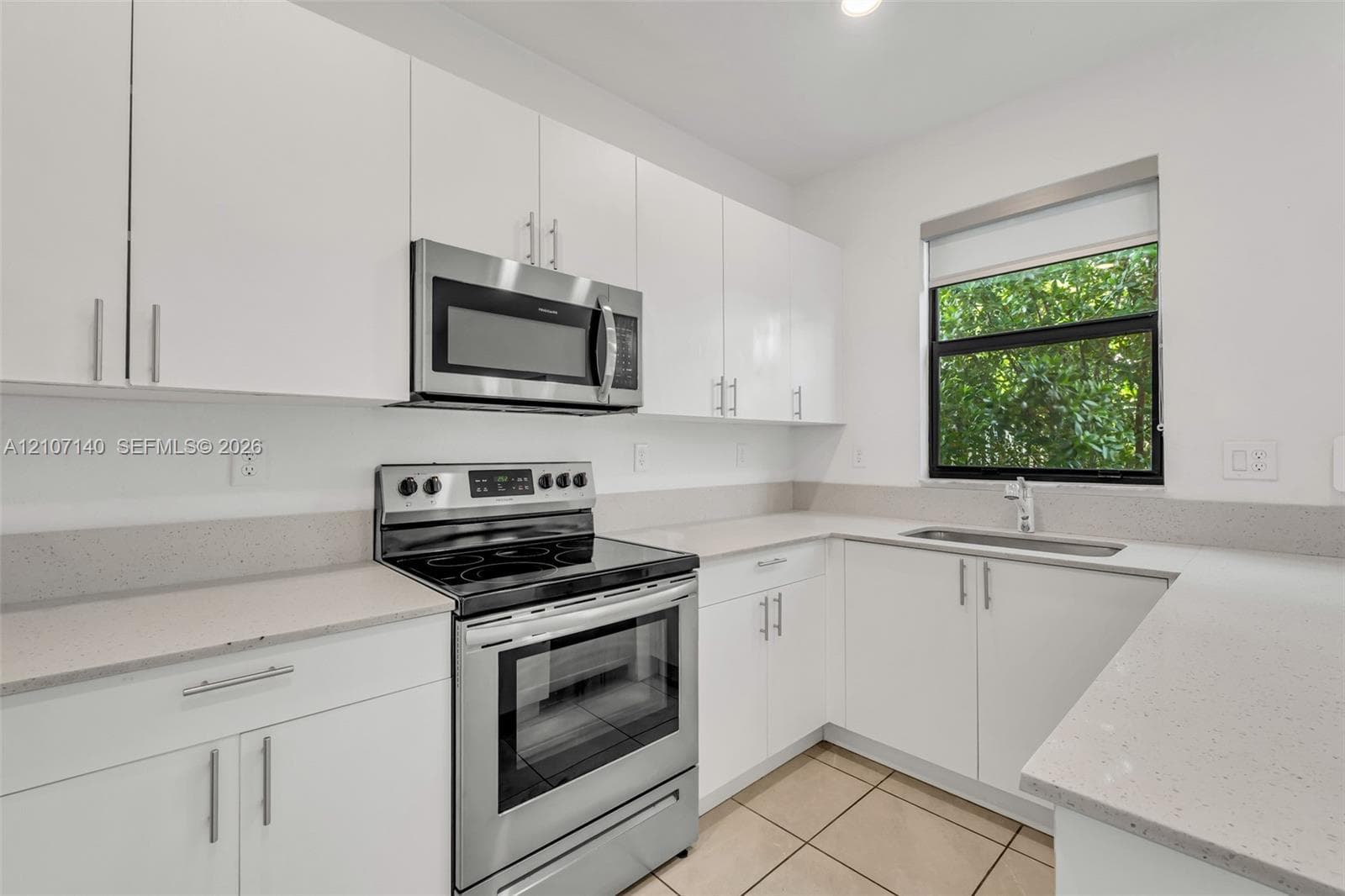 Kitchen featuring white flat-panel cabinetry, light-toned composite countertops, stainless steel appliances, and tile flooring