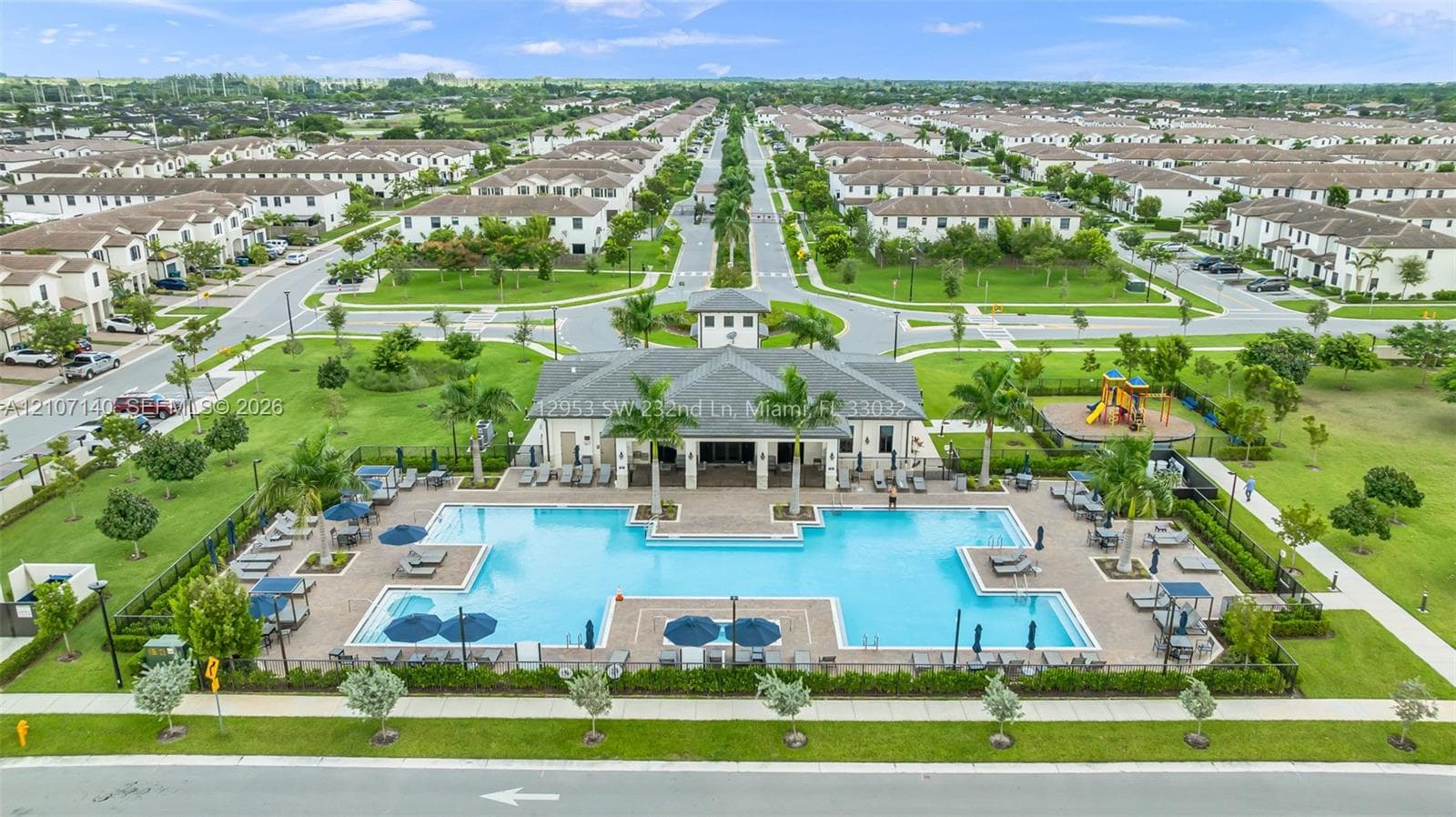 Community clubhouse featuring a large swimming pool, paved pool deck, and outdoor recreational area with playground equipment