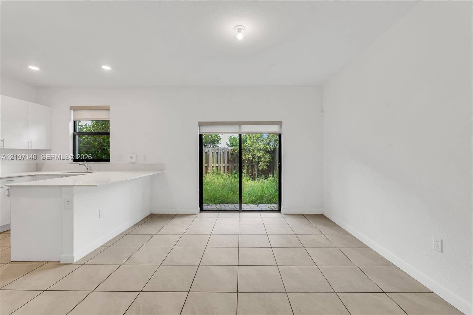 Open-concept interior featuring light-colored tile flooring, white cabinetry, a kitchen island with a stone-finish countertop, and sliding glass doors