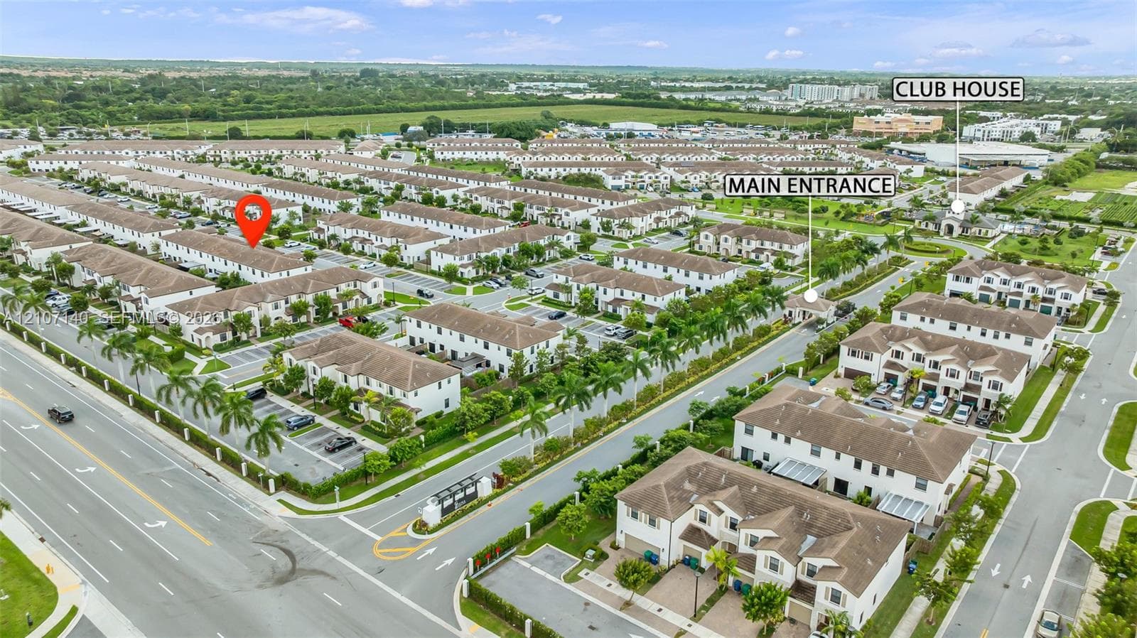 Aerial perspective of a multi-unit residential community featuring paved thoroughfares, organized surface parking, palm tree landscaping, and a gated entrance