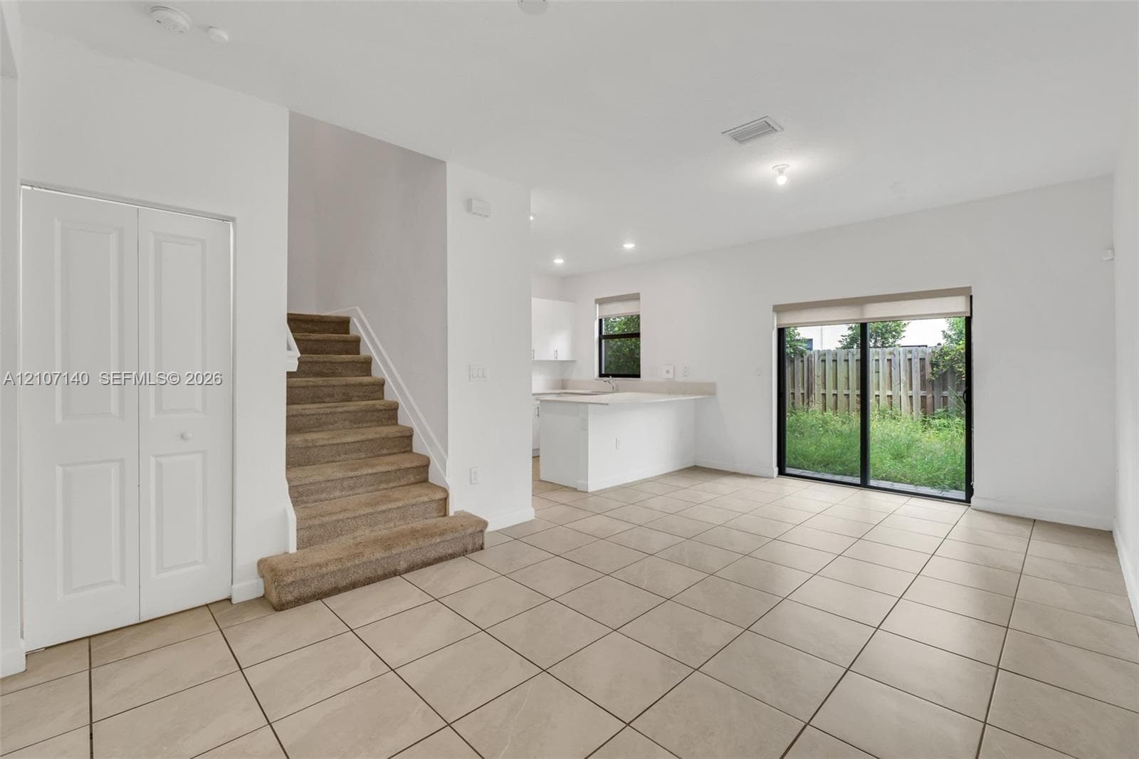 Open-concept floor plan with ceramic tile flooring, kitchen island, carpeted staircase, and sliding glass doors