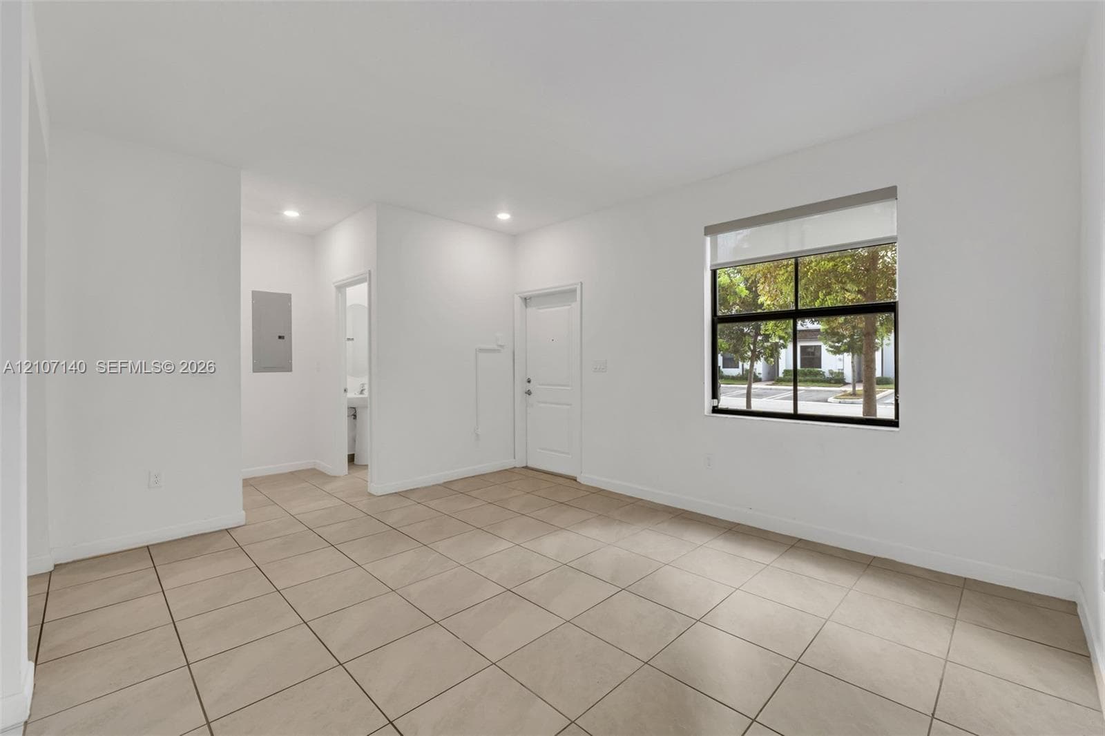 Neutral interior featuring large-format ceramic tile flooring, recessed lighting, and a single-pane window with a roller shade