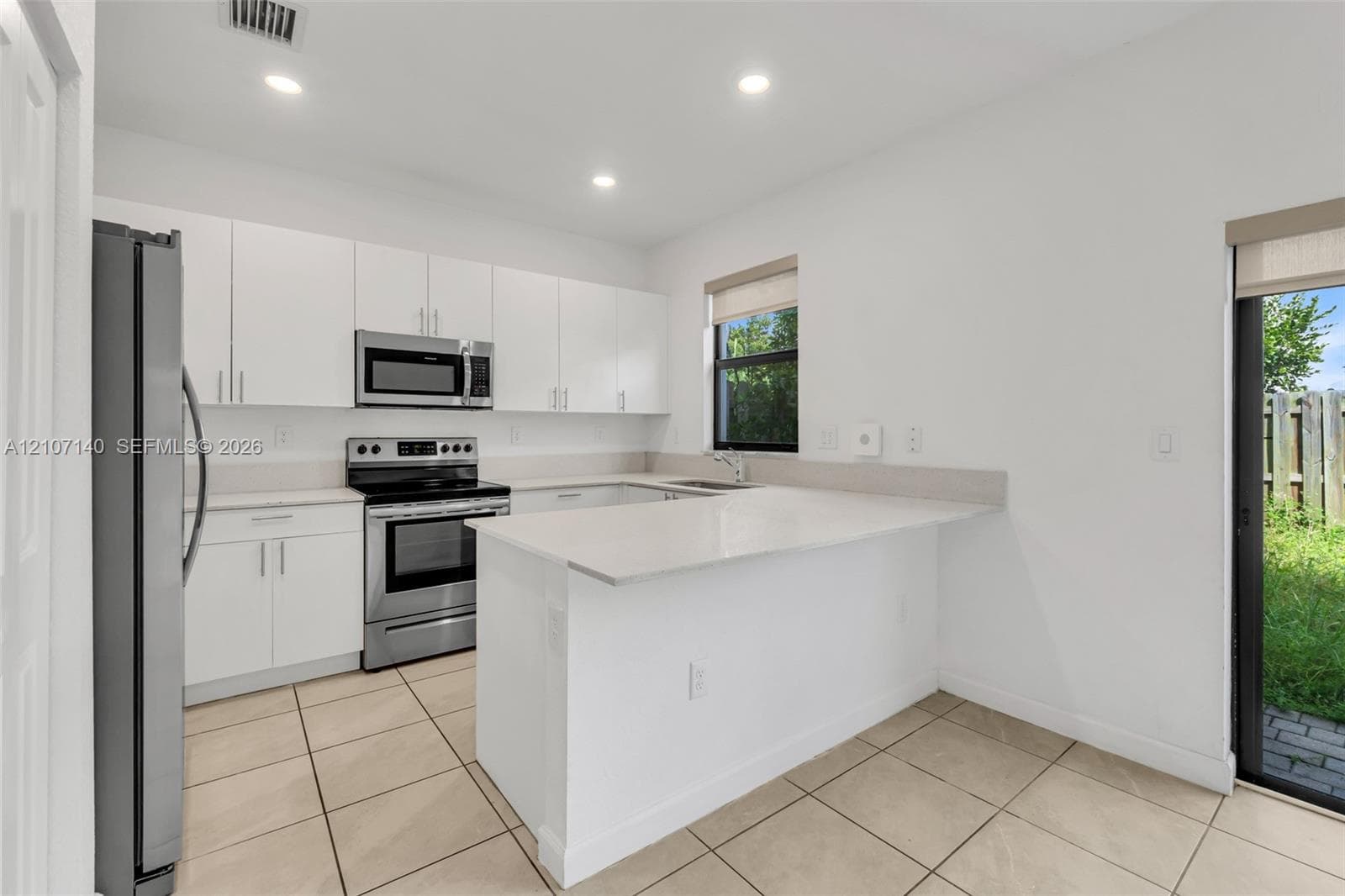 Kitchen featuring white flat-panel cabinetry, stainless steel appliances, a peninsula with stone-surface countertop, and ceramic tile flooring