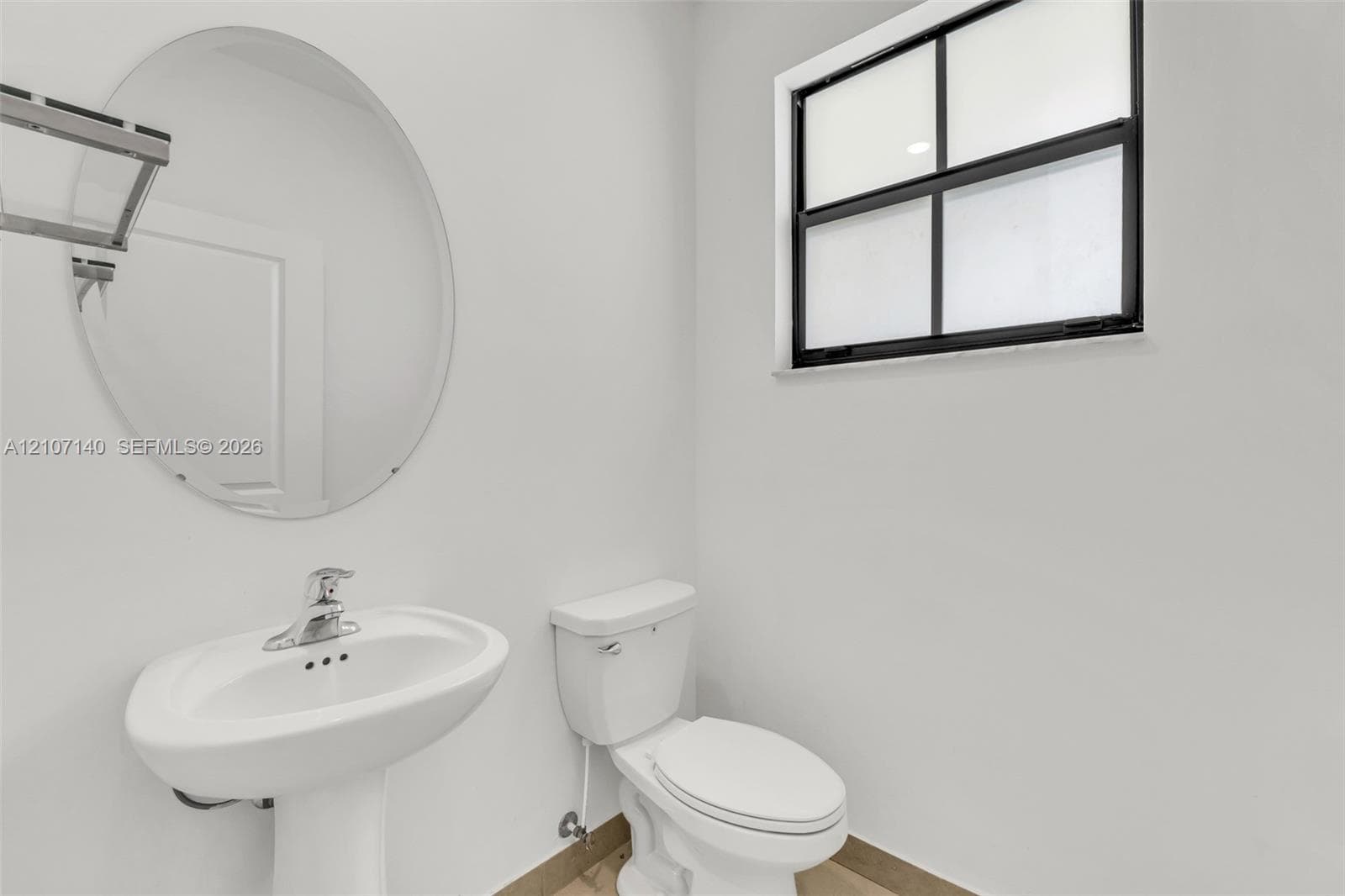 Wall-mounted oval mirror, pedestal sink with chrome faucet, and multi-pane window with black frame