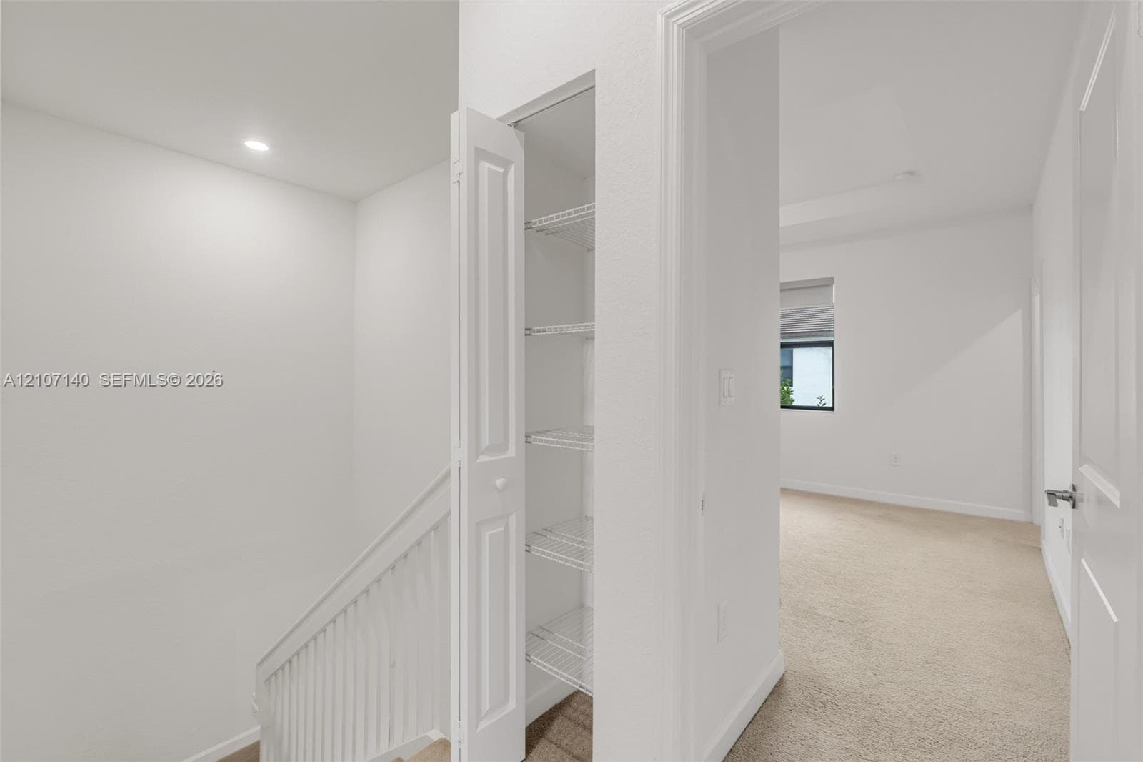Built-in storage closet with wire shelving, white paneled door, neutral carpeting, and white balustrade railing