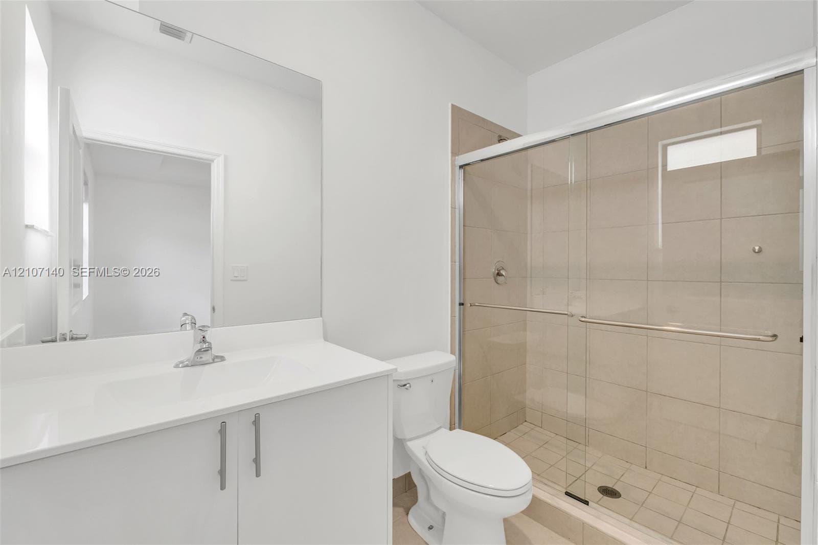White vanity with integrated sink, chrome faucet, full-width mirror, and walk-in shower featuring a glass enclosure and tiled walls