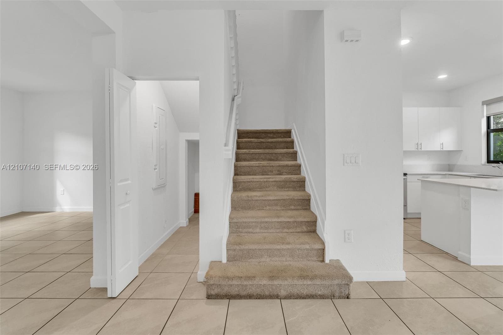 Interior staircase featuring carpeted treads, neutral-tone tile flooring, and white cabinetry