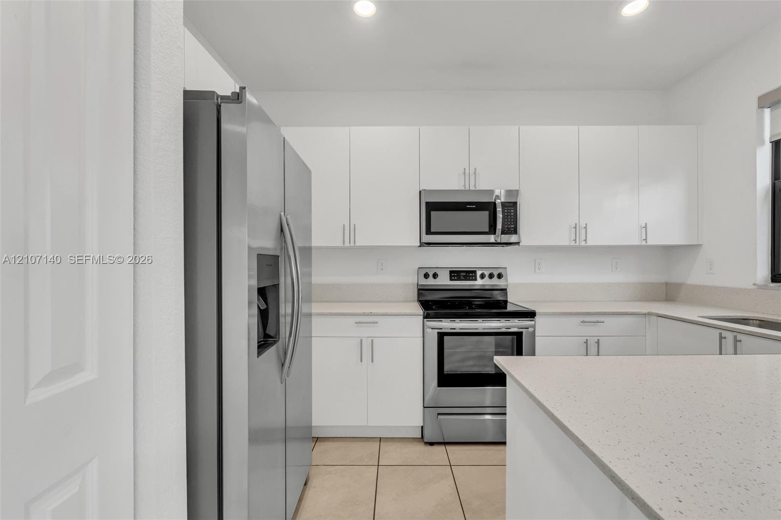 Kitchen featuring white cabinetry, solid-surface countertops, tile flooring, and stainless steel appliances