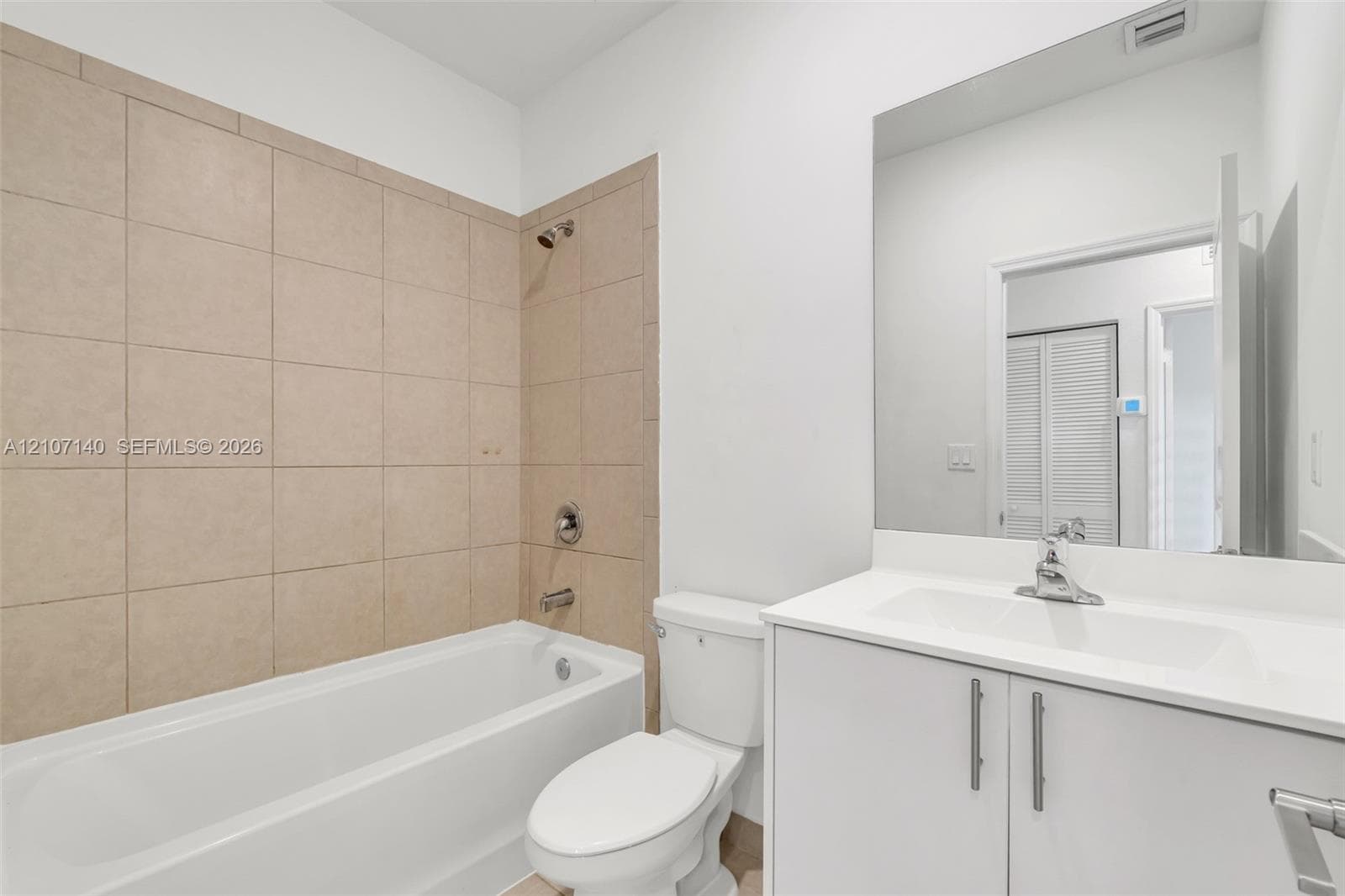 Bathroom featuring a white vanity cabinet with a solid-surface countertop, an integrated sink, full-width mirror, and a tub-shower combination with floor-to-ceiling neutral tile surround