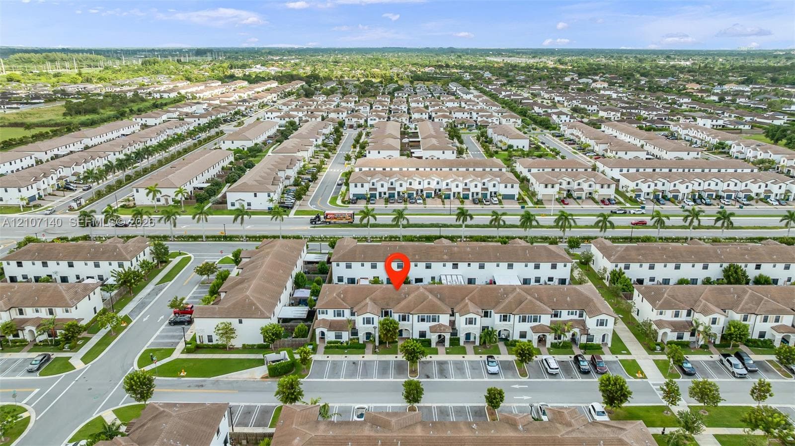 Aerial perspective of a multi-unit residential building featuring a light-toned stucco exterior, shingled roof lines, and dedicated surface parking