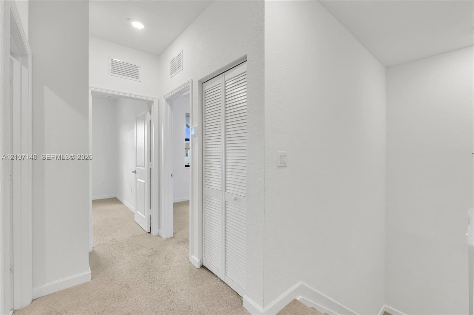 Hallway featuring neutral carpeting, white interior doors, and a louvered bi-fold closet door