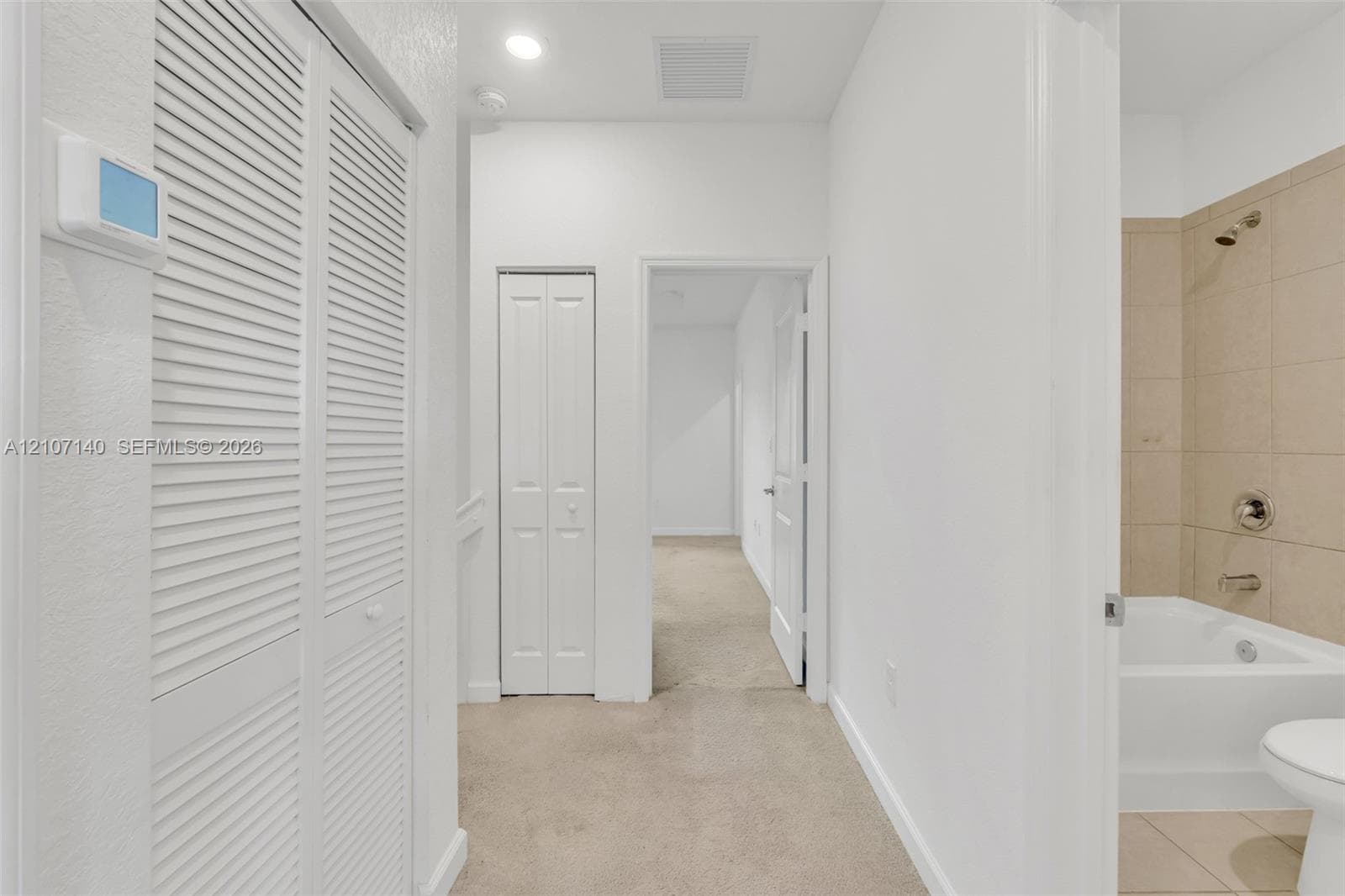 Hallway featuring dual bifold closets, neutral carpeting, recessed ceiling lighting, and a bathroom equipped with a porcelain tub, showerhead, and wall-mounted plumbing fixtures