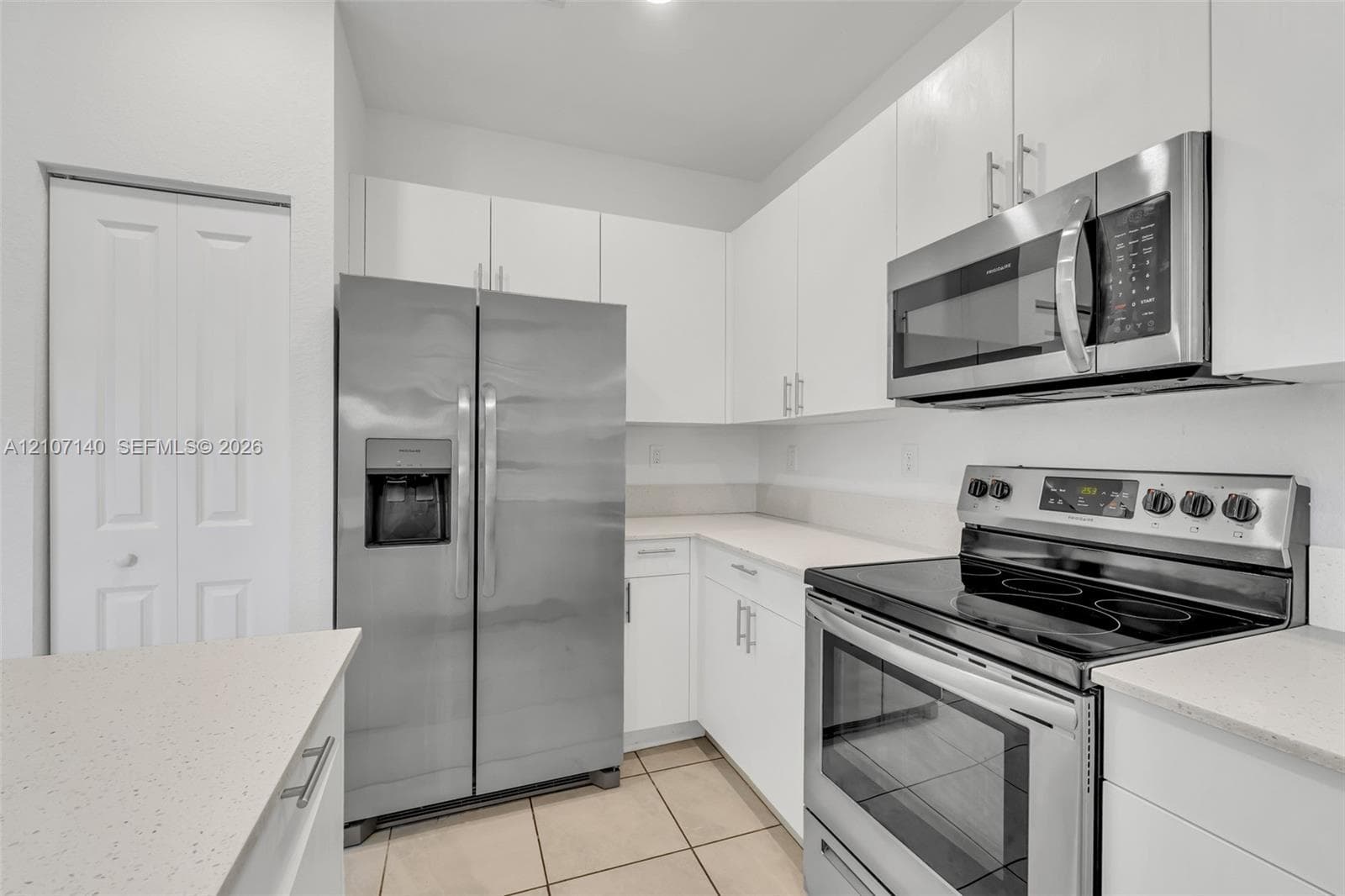Kitchen featuring white cabinetry, solid-surface countertops, stainless steel appliances, and tiled flooring
