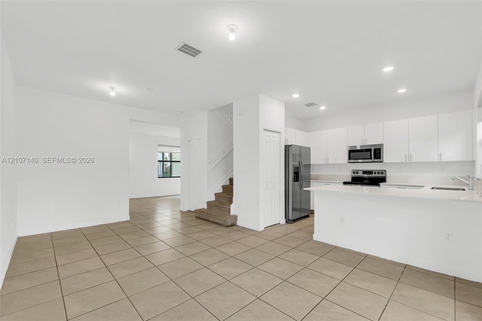Kitchen featuring white cabinetry, solid-surface countertops, and stainless steel appliances, complemented by tile flooring and recessed lighting
