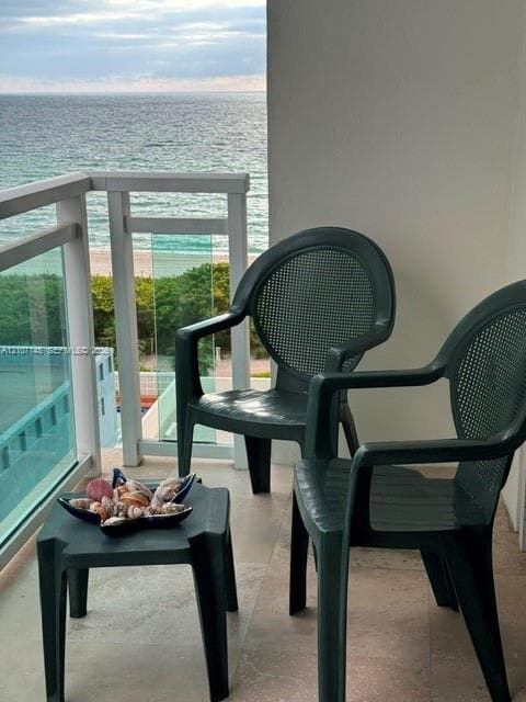 Covered balcony featuring stone-finish flooring and glass-panel railing overlooking the coastline