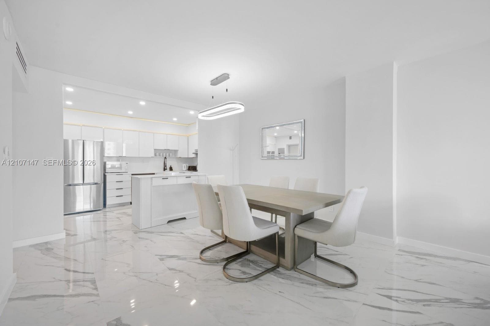 Polished stone-finish flooring, kitchen island with built-in cabinetry, stainless steel refrigerator, and modern oval-shaped pendant lighting