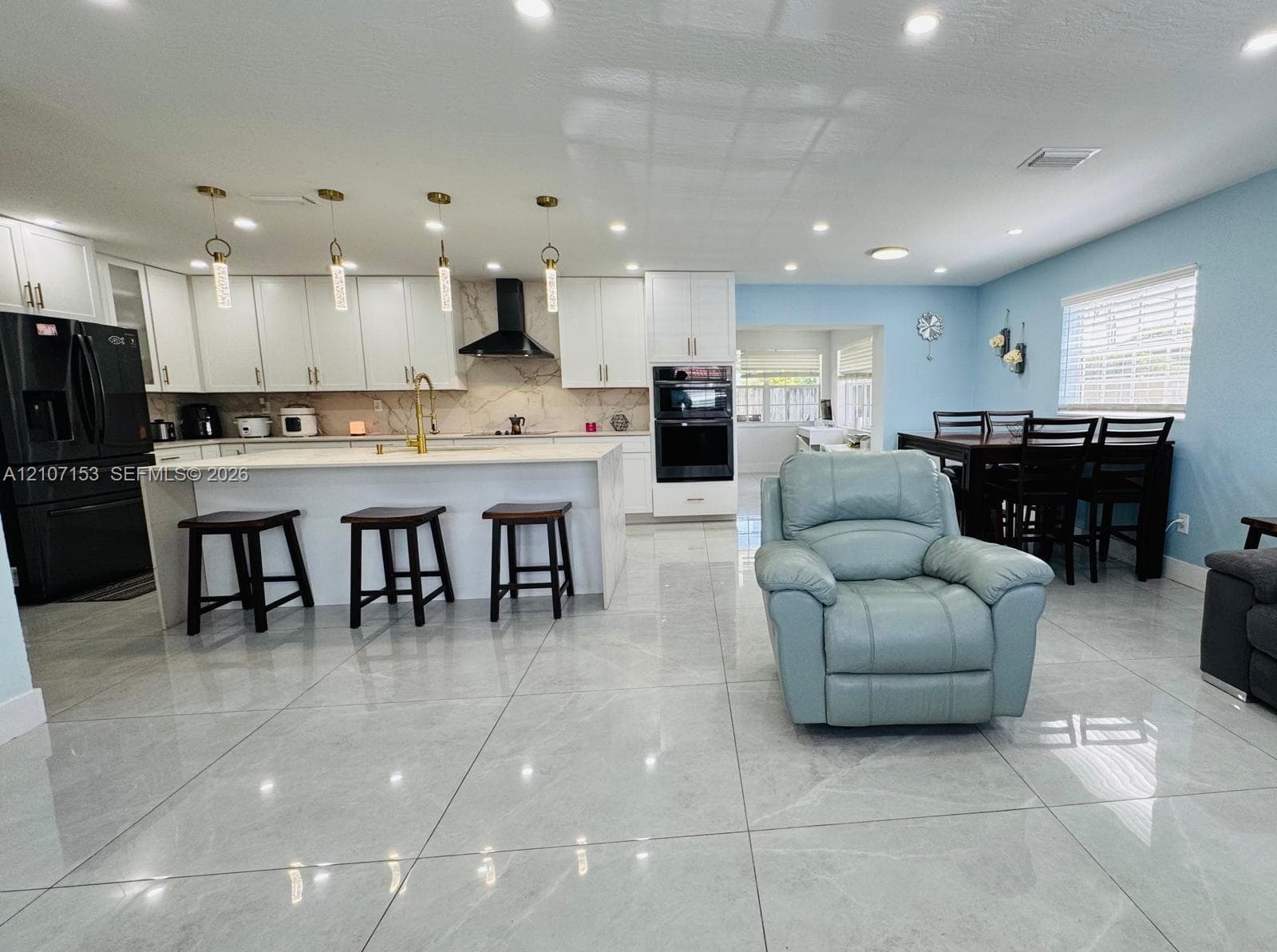 Kitchen featuring white shaker-style cabinetry, a stone-surfaced waterfall island, built-in double wall ovens, recessed lighting, and large-format tile flooring