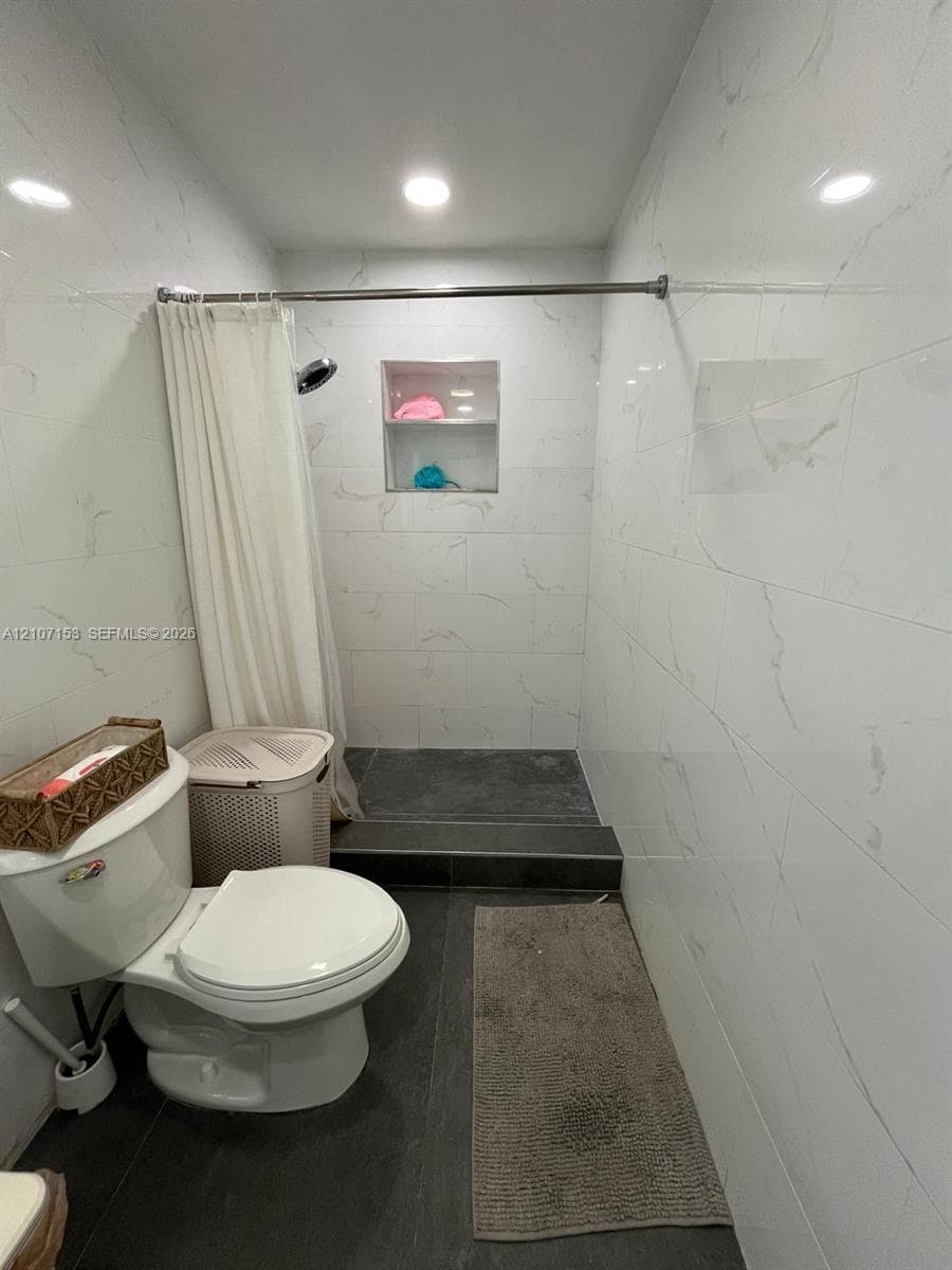 Bathroom featuring white wall tiling with grey veining, a built-in recessed shower niche, and dark-toned floor tiling
