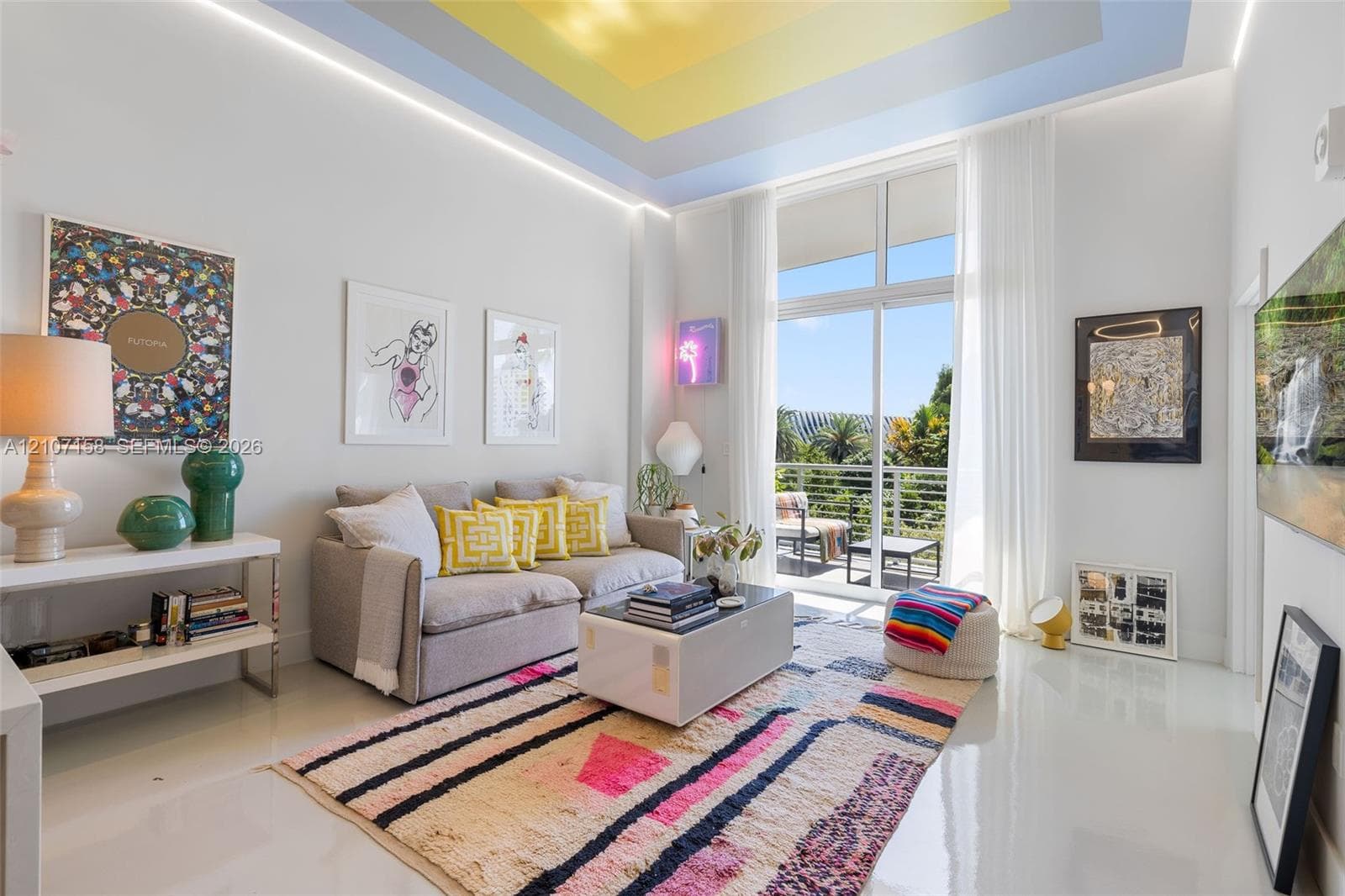 High-ceilinged living area featuring a recessed tray ceiling with multi-colored tiered detail, integrated perimeter lighting, high-gloss flooring, and floor-to-ceiling glass sliding doors opening to a balcony