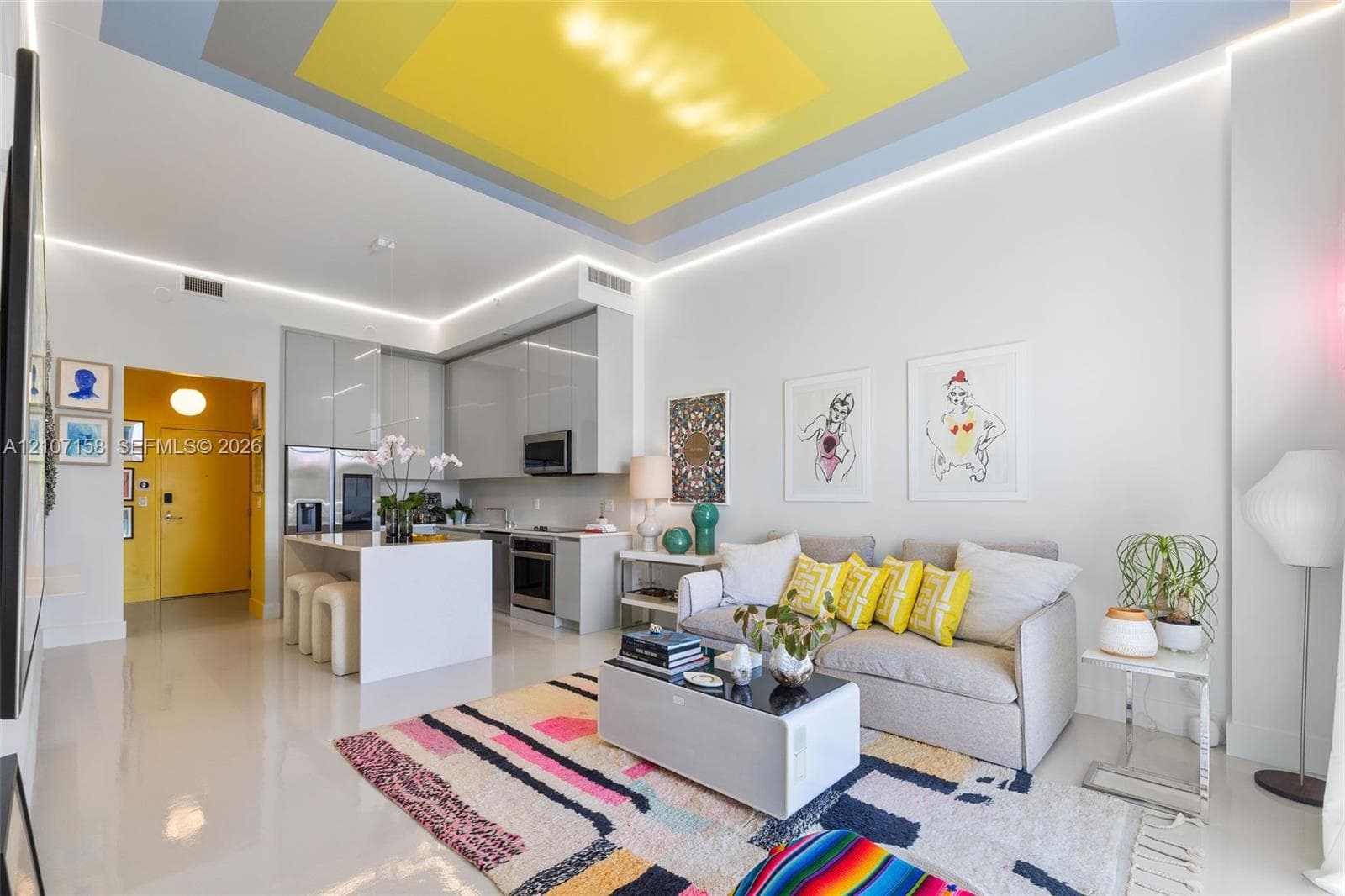 Open-concept living space featuring high-gloss flooring, recessed linear perimeter lighting, a geometric multi-tone ceiling design, and a kitchen with custom flat-panel cabinetry and a white solid-surface island