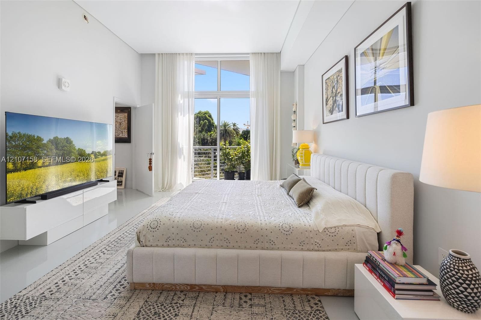 Floor-to-ceiling windows, high ceilings, wall-mounted floating cabinetry, and a balcony with a metal railing