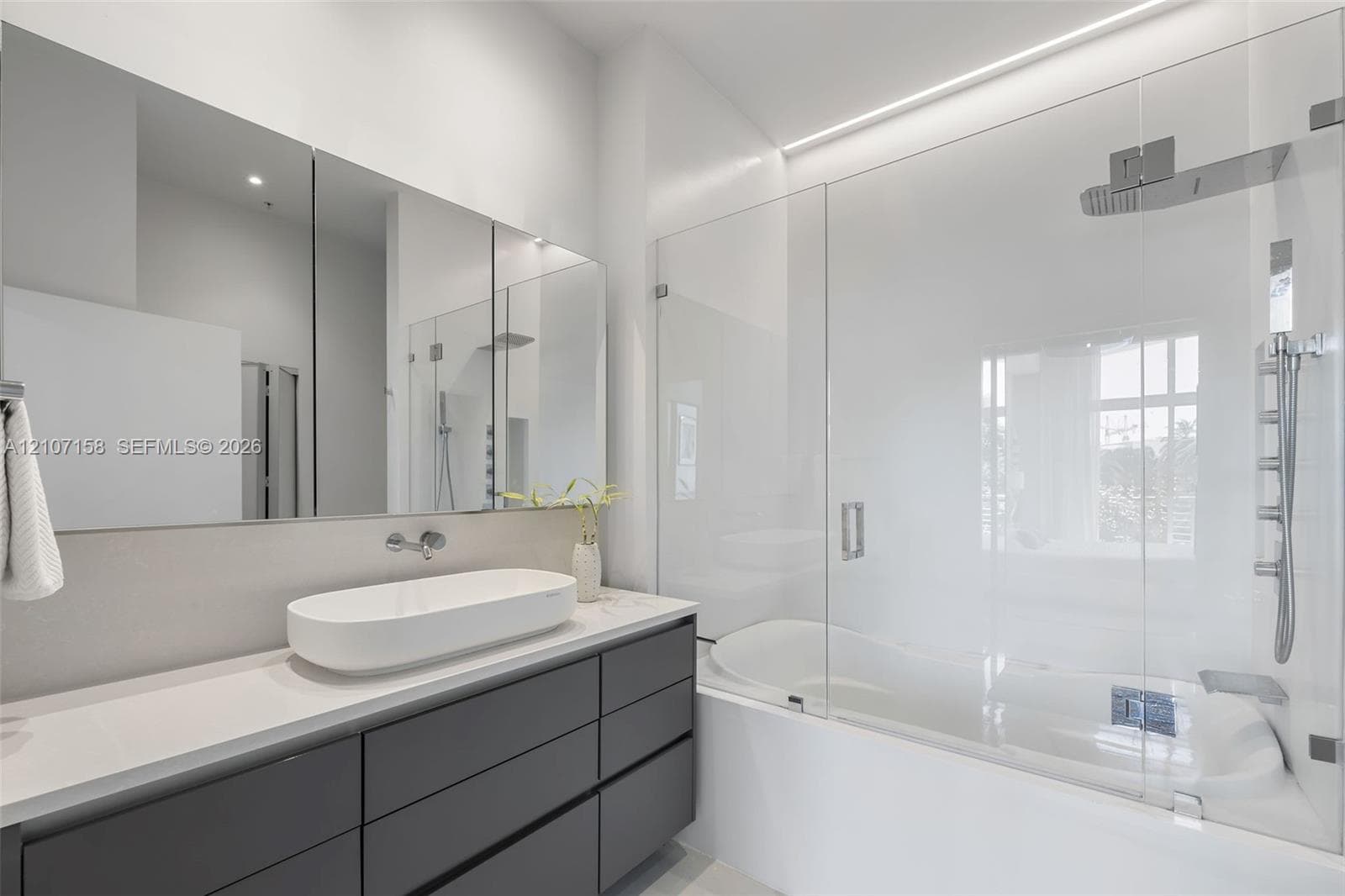 Modern vanity with charcoal cabinetry, rectangular vessel sink, white countertop, full-width mirror, and glass-enclosed shower-tub combination with chrome fixtures