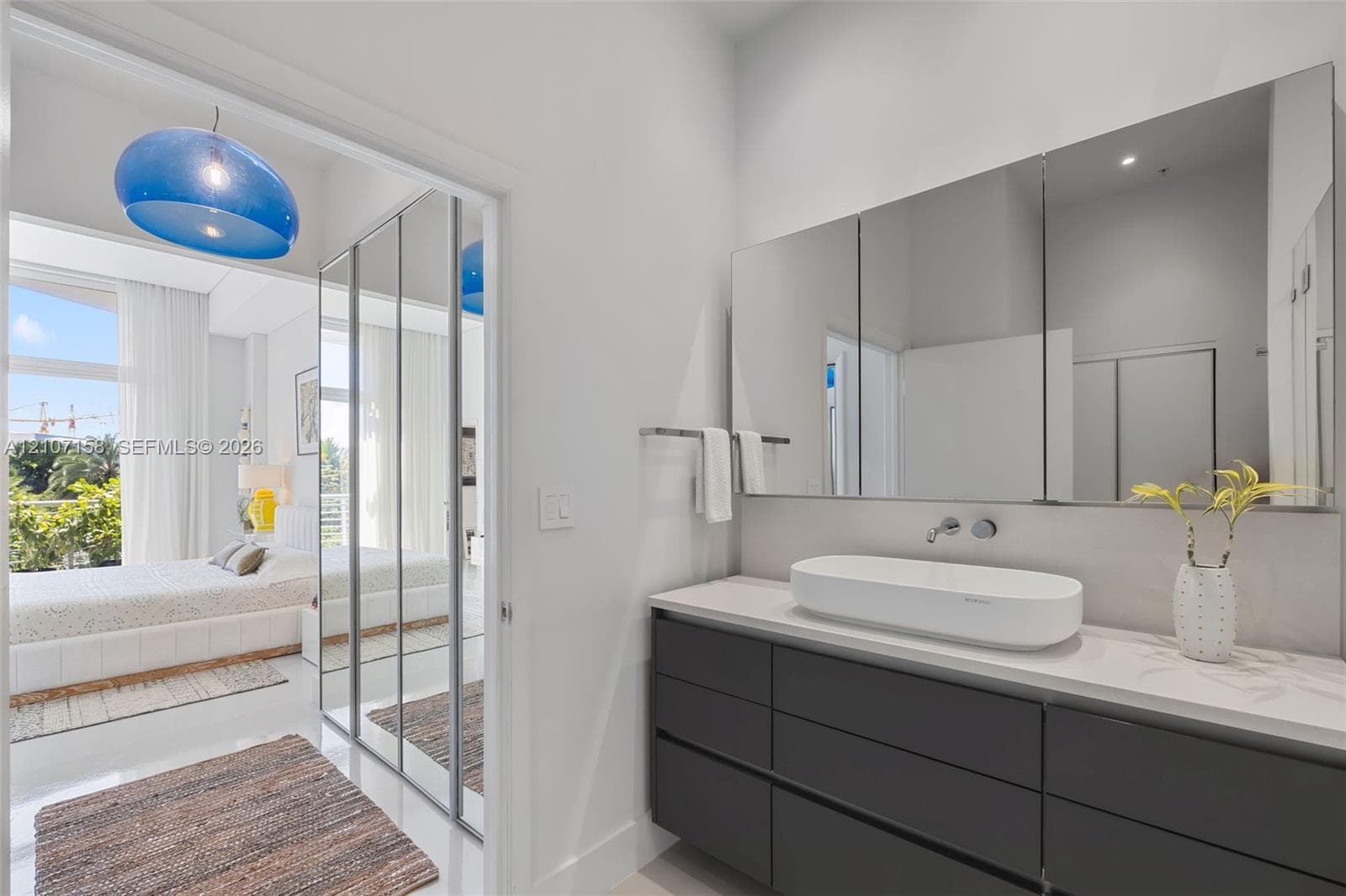 Bathroom vanity featuring a dark-toned flat-panel cabinet, white countertop, oval vessel sink, wall-mounted faucet, and a large multi-paneled mirror cabinet