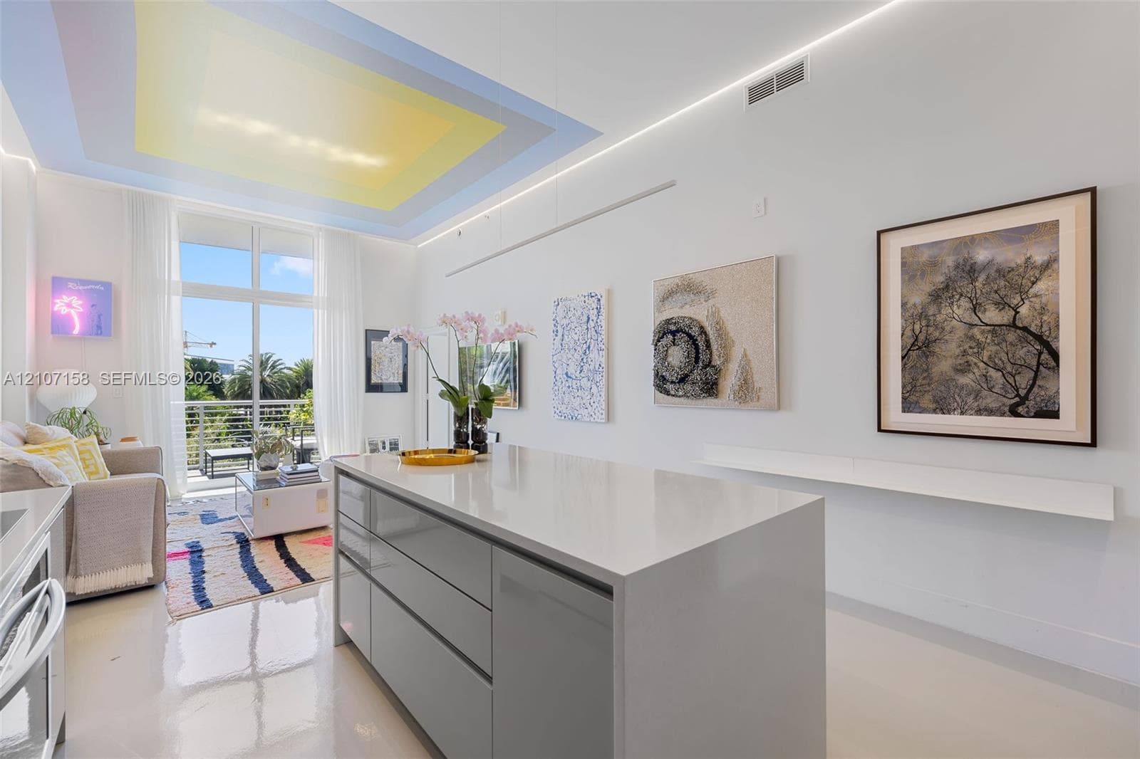 Kitchen island featuring a stone countertop and handleless cabinetry, recessed ceiling lighting, and floor-to-ceiling glass door opening to a balcony