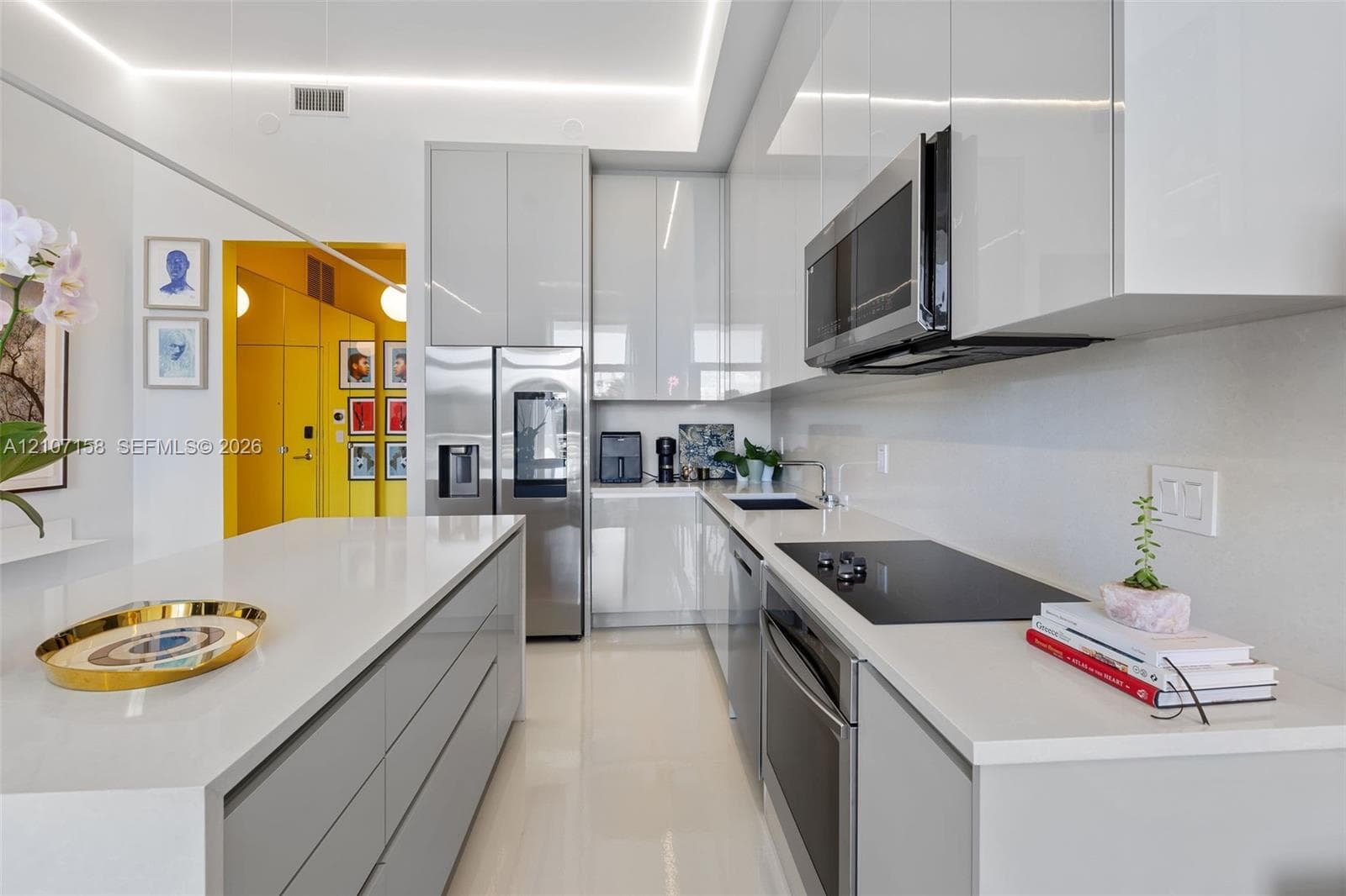 Kitchen featuring high-gloss cabinetry, stone countertops, stainless steel appliances, a central island, and recessed cove lighting