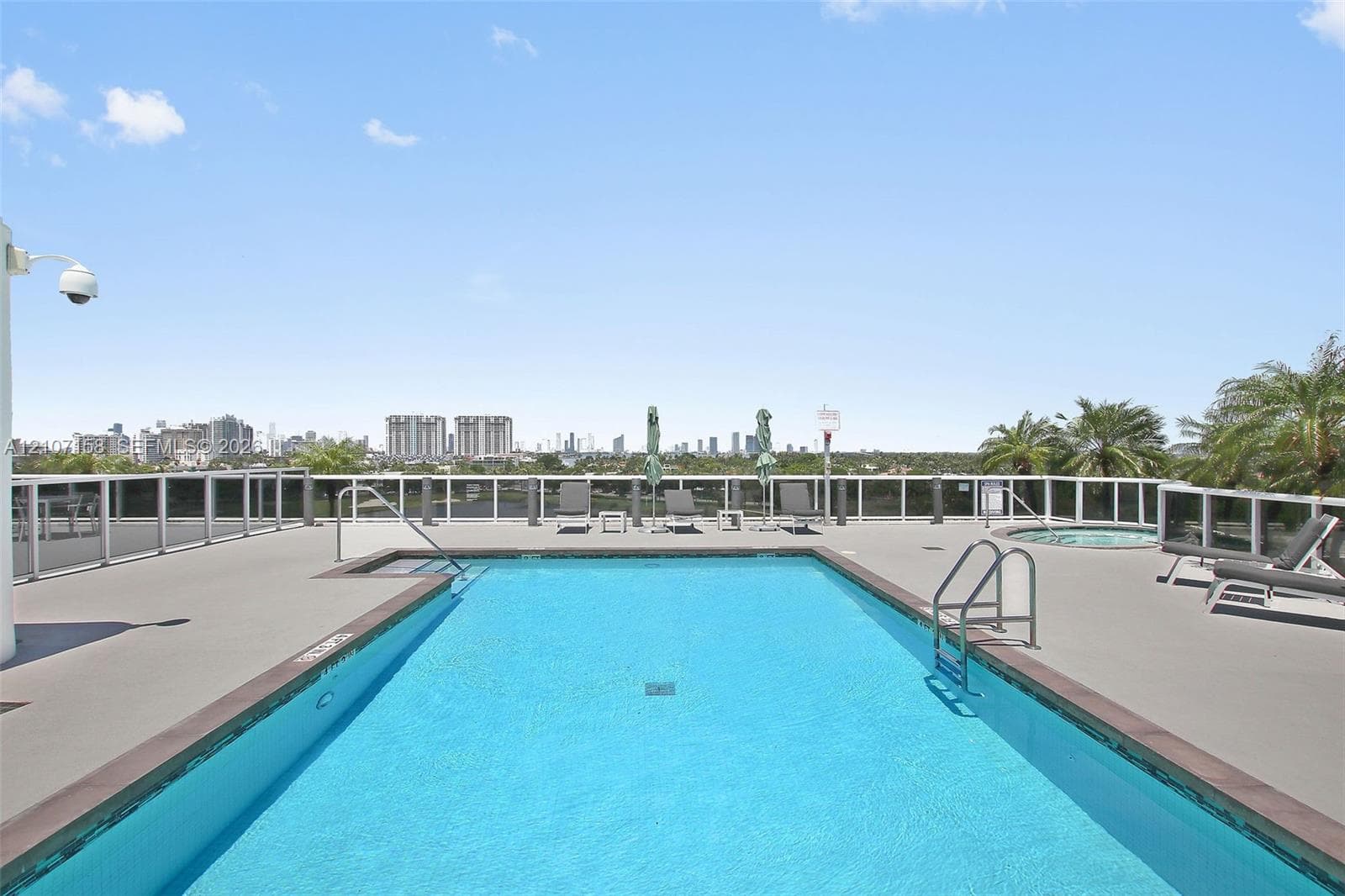 Rooftop swimming pool and spa featuring a concrete deck, white metal railings, and stainless steel pool ladders