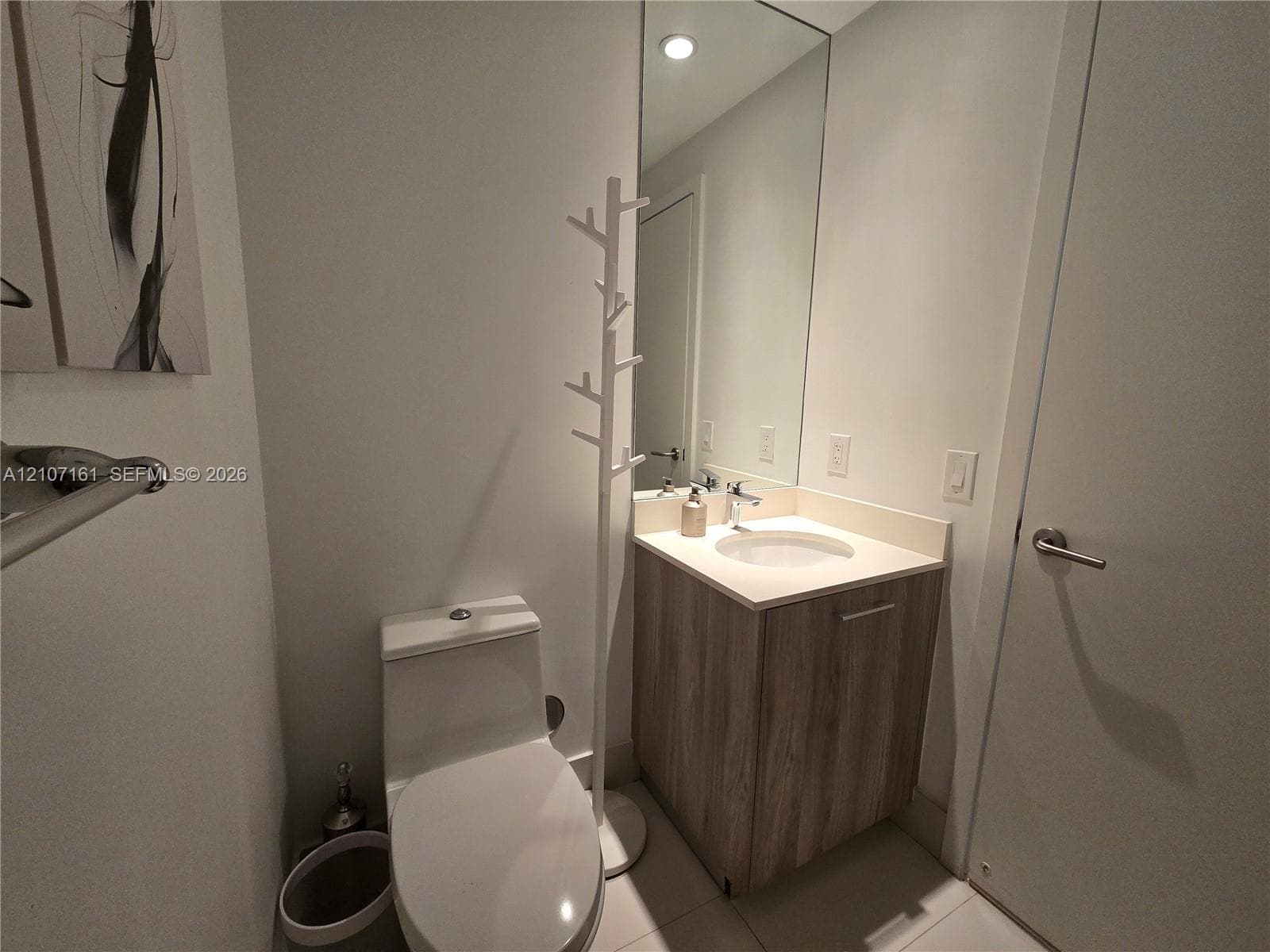 Single-flush toilet, vanity with wood-finish cabinetry, solid-surface countertop, integrated basin, and large-format wall mirror