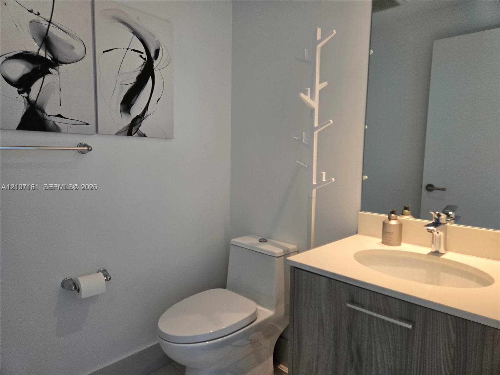Vanity featuring a light wood-finish cabinet with an integrated countertop and sink, chrome fixtures, and a large-format frameless wall mirror