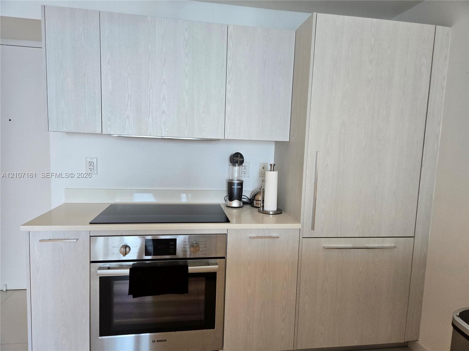 Light-toned wood-finish cabinetry, solid-surface countertops, built-in panel-ready refrigerator, and integrated stainless steel oven with a smooth-top cooktop