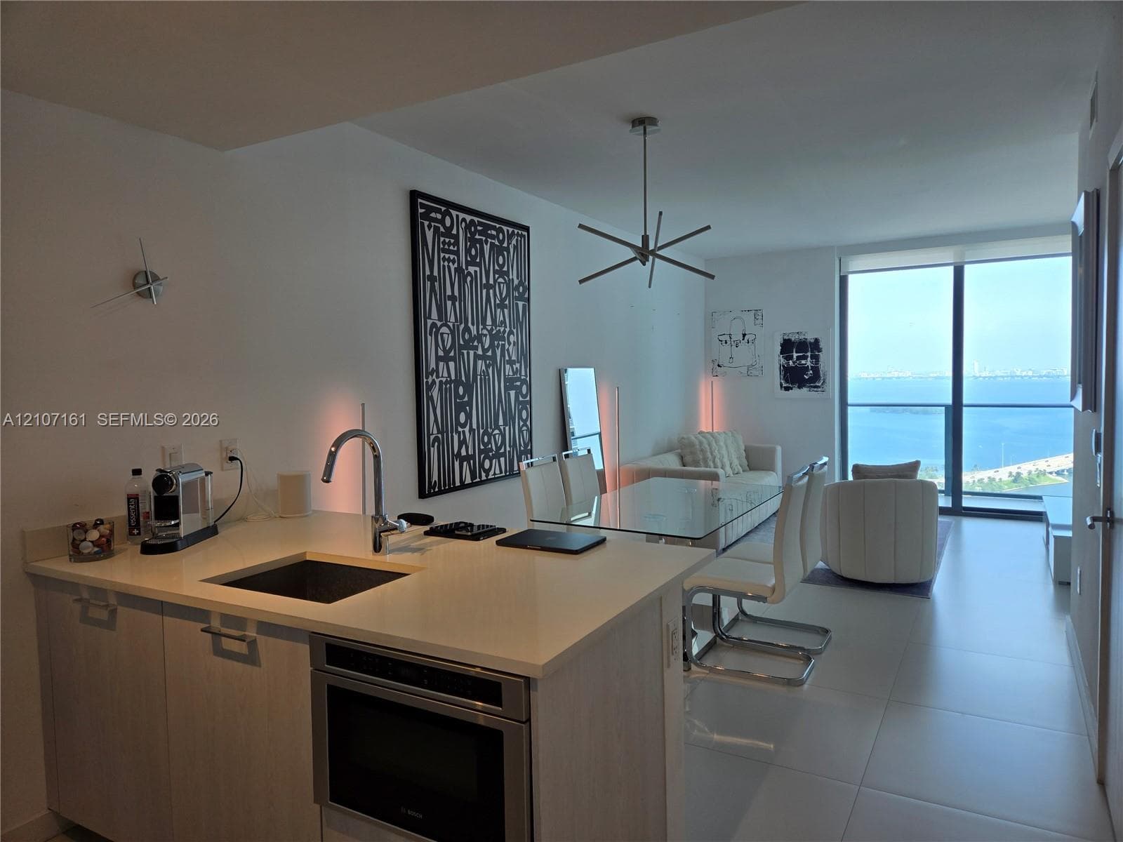 Kitchen featuring light-toned cabinetry, solid surface countertops, a stainless steel undermount sink with a gooseneck faucet, and a built-in microwave, complemented by floor-to-ceiling windows with water scenery
