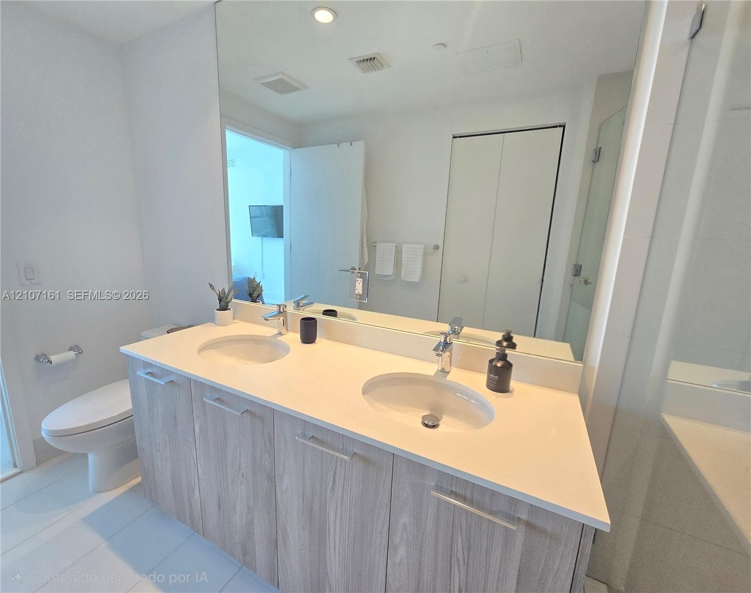 Dual-sink vanity with light wood-finish cabinetry, solid-surface countertop, and full-width wall mirror